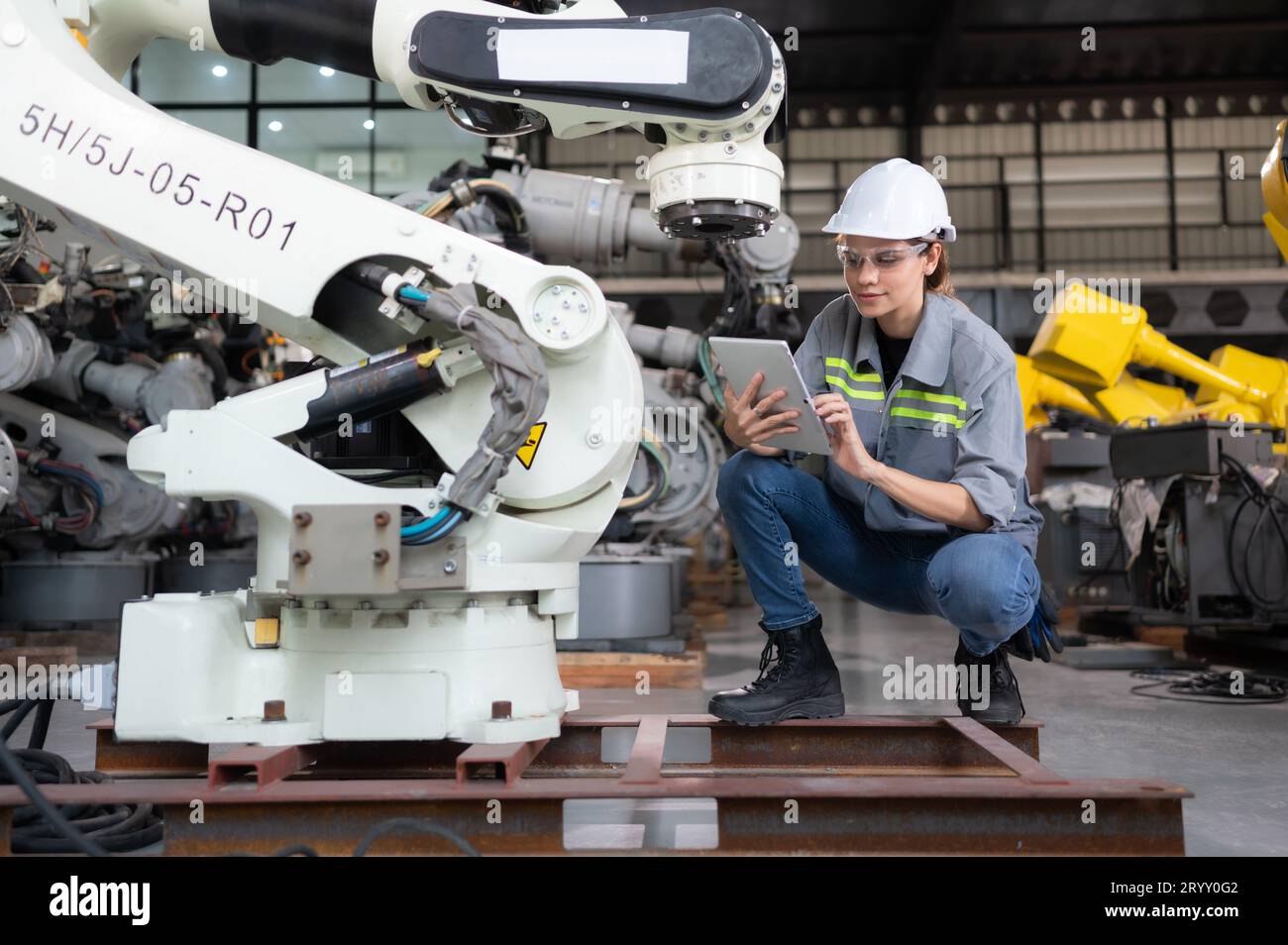 A female engineer installs a program on a robotics arm in a robot warehouse. And test the operation before sending the machine t Stock Photo