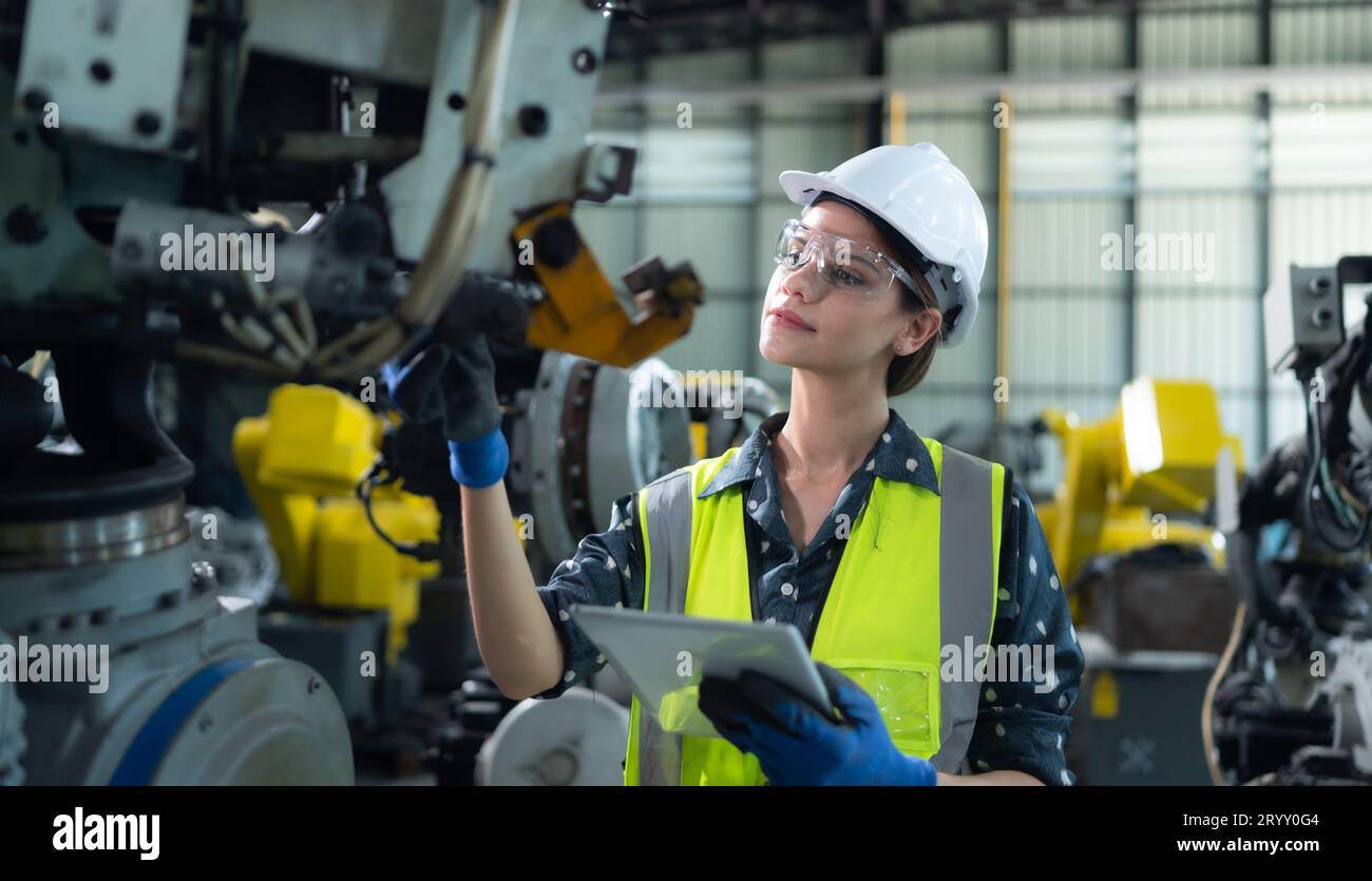 A female engineer installs a program on a robotics arm in a robot warehouse. And test the operation before sending the machine t Stock Photo