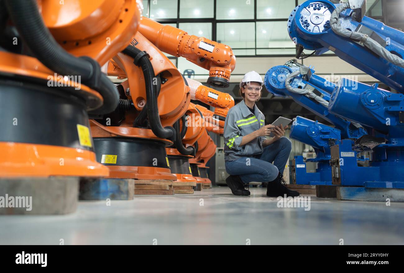 A female engineer installs a program on a robotics arm in a robot warehouse. And test the operation before sending the machine t Stock Photo