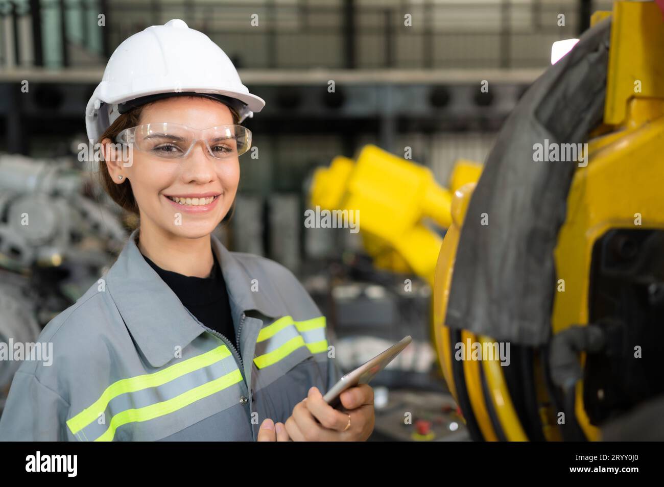 A female engineer installs a program on a robotics arm in a robot warehouse. And test the operation before sending the machine t Stock Photo