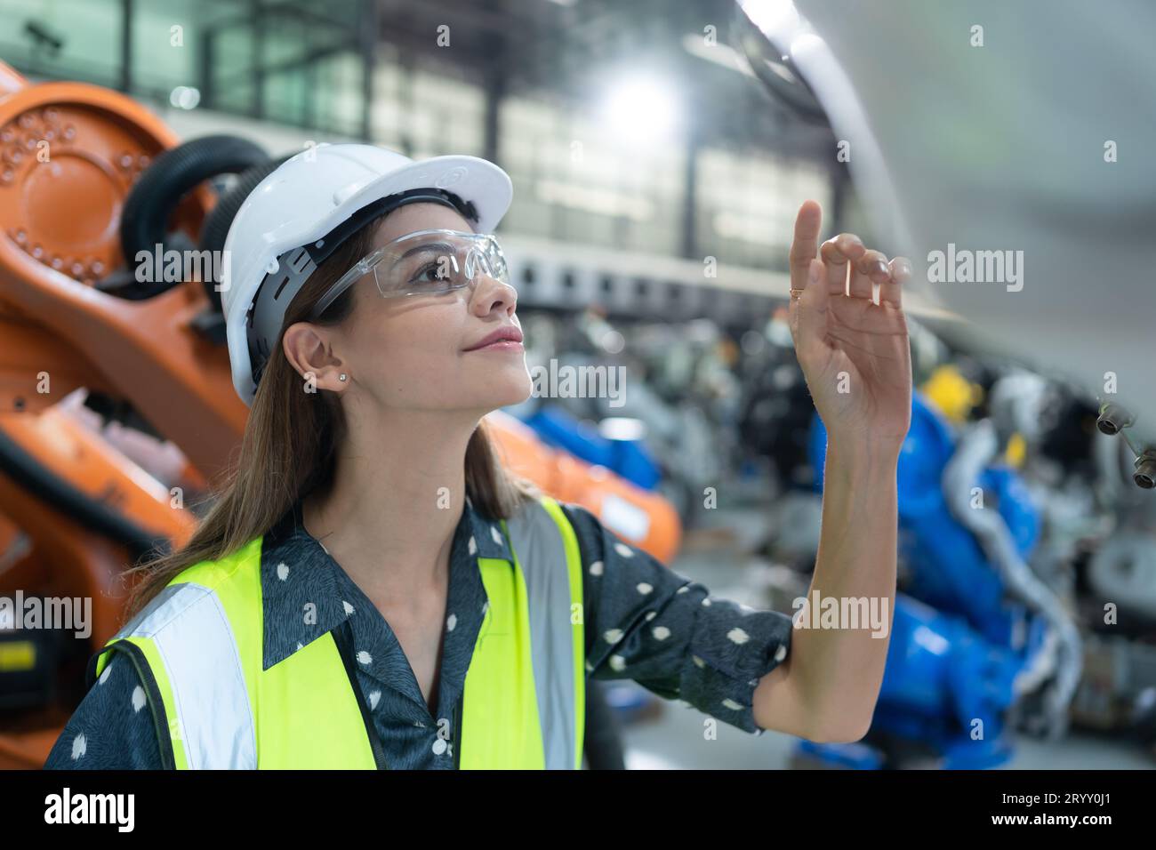 A female engineer installs a program on a robotics arm in a robot warehouse. And test the operation before sending the machine t Stock Photo