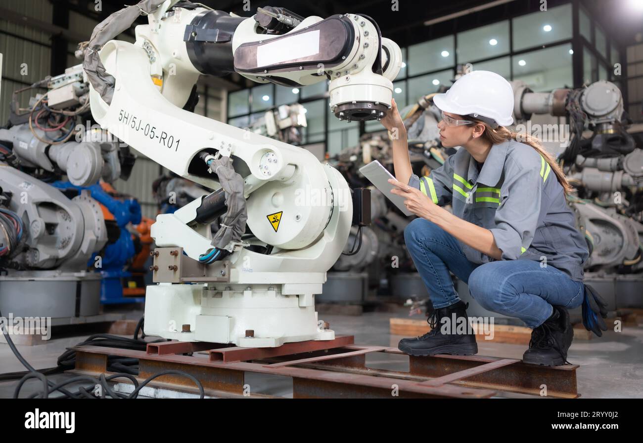 A female engineer installs a program on a robotics arm in a robot warehouse. And test the operation before sending the machine t Stock Photo