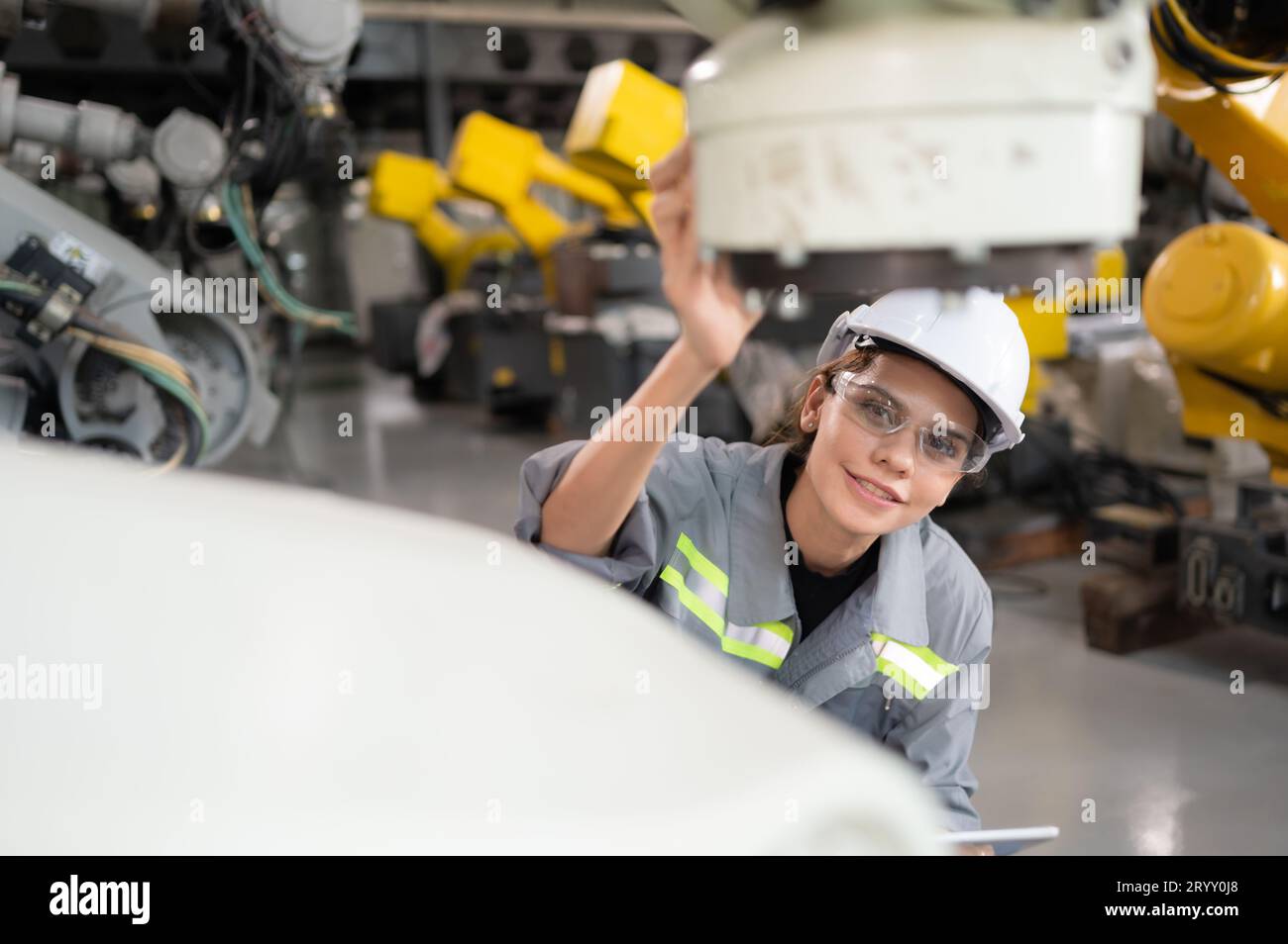 A female engineer installs a program on a robotics arm in a robot warehouse. And test the operation before sending the machine t Stock Photo