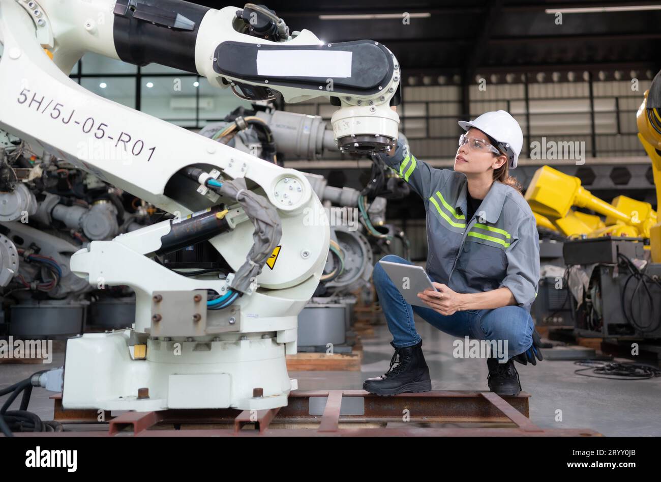 A female engineer installs a program on a robotics arm in a robot warehouse. And test the operation before sending the machine t Stock Photo