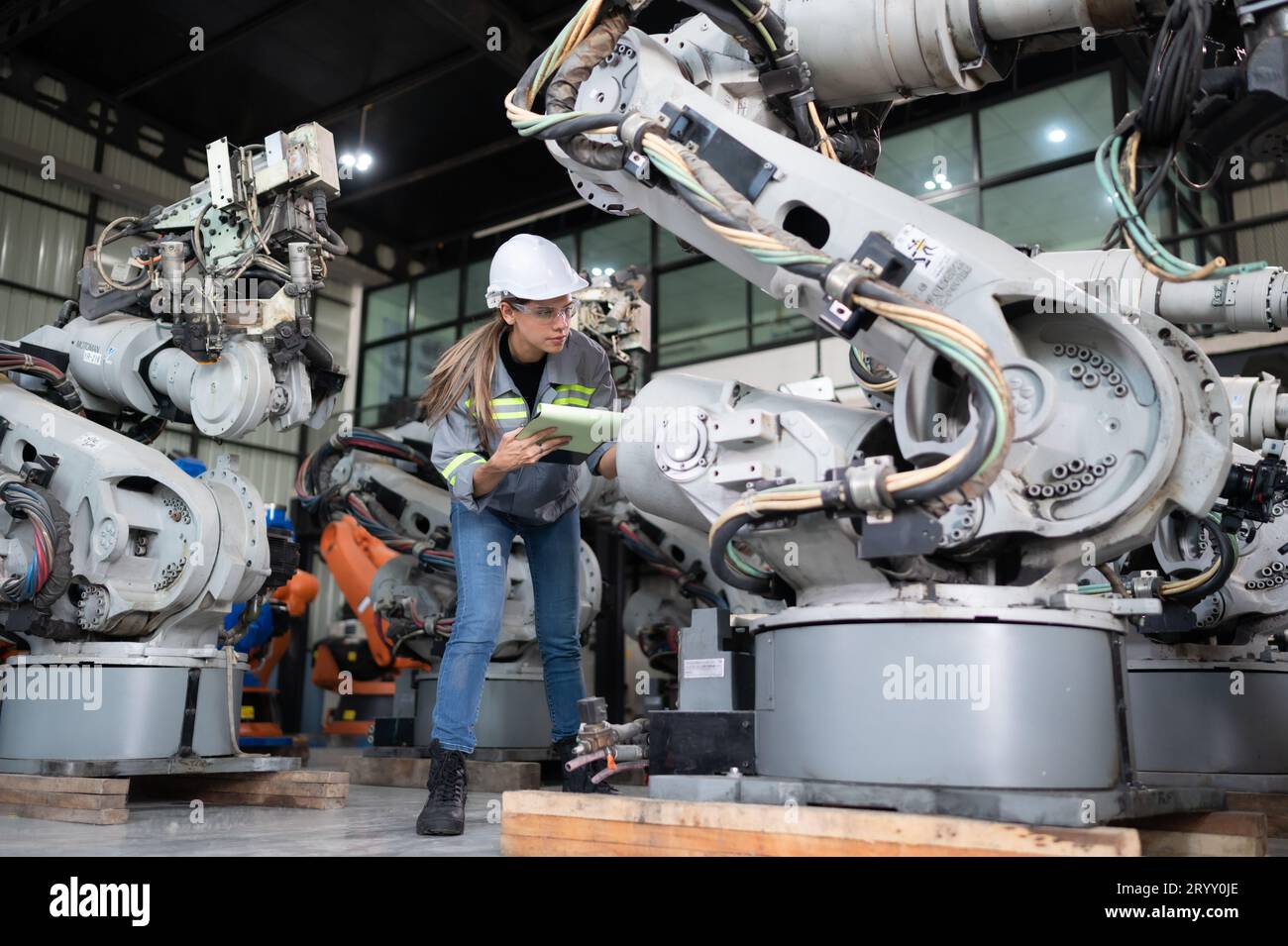 A female engineer checking documented items after installing a program on a robotic arm in a robotic warehouse and test the oper Stock Photo