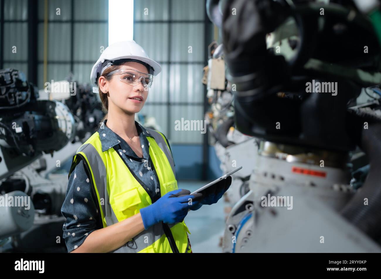 A female engineer installs a program on a robotics arm in a robot warehouse. And test the operation before sending the machine t Stock Photo