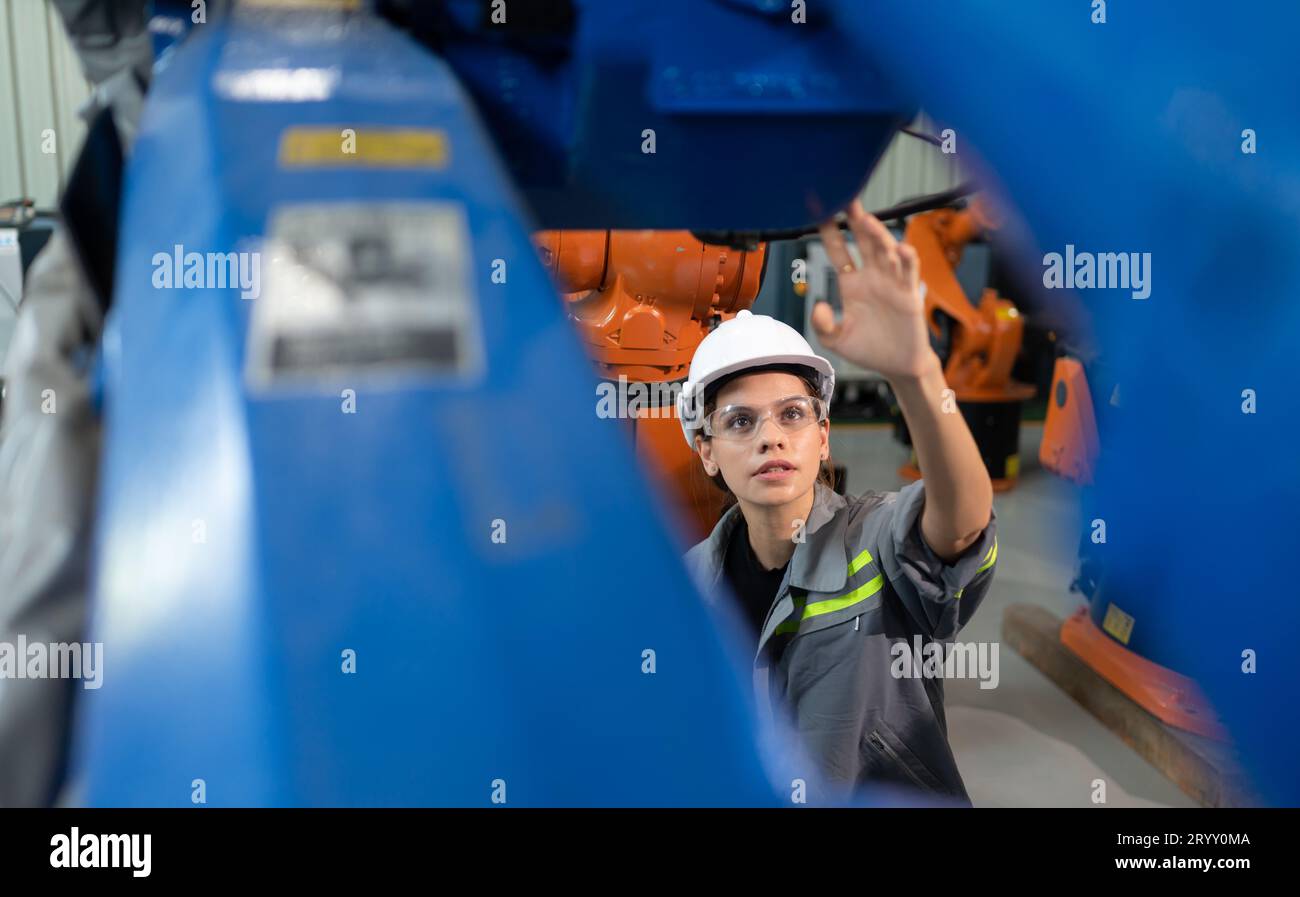 A female engineer installs a program on a robotics arm in a robot warehouse. And test the operation before sending the machine t Stock Photo