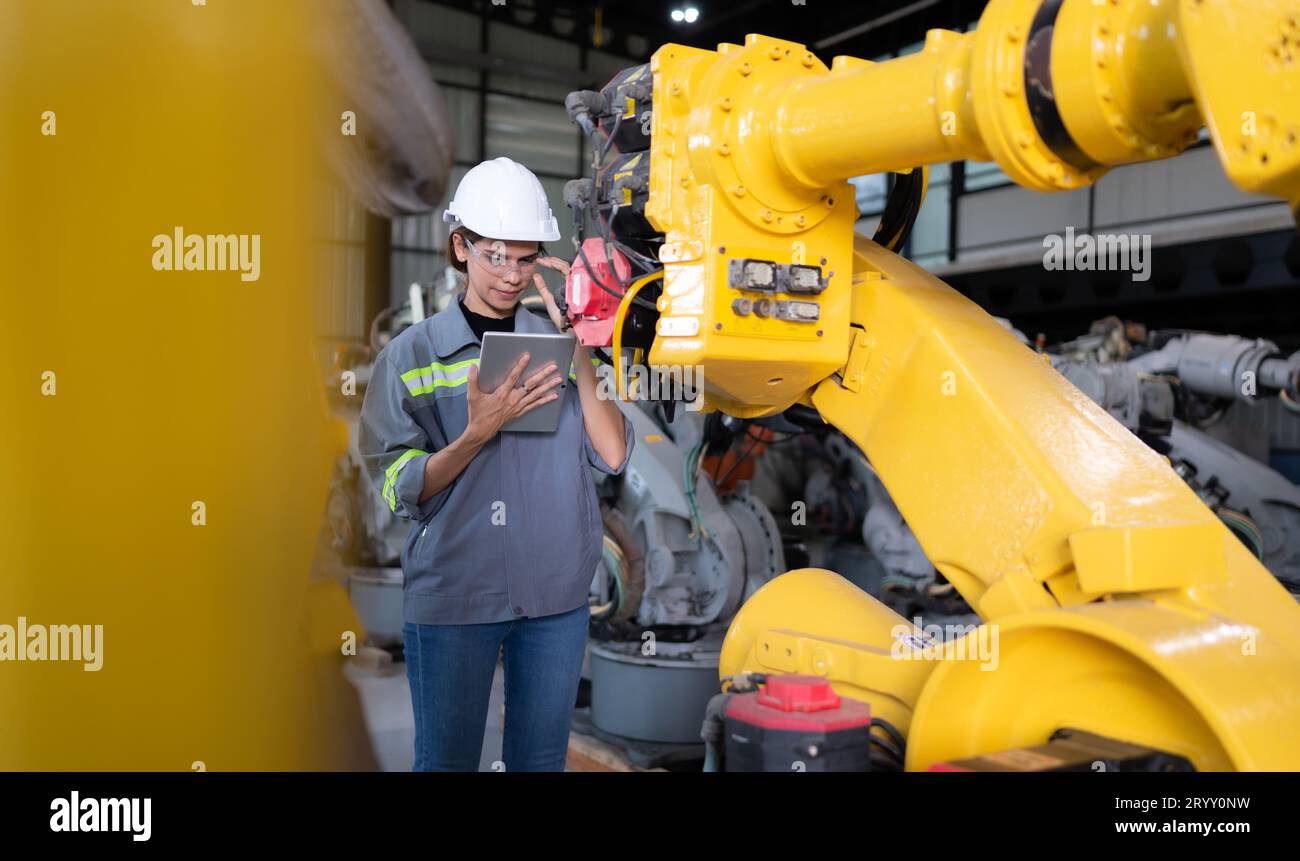 A female engineer installs a program on a robotics arm in a robot warehouse. And test the operation before sending the machine t Stock Photo