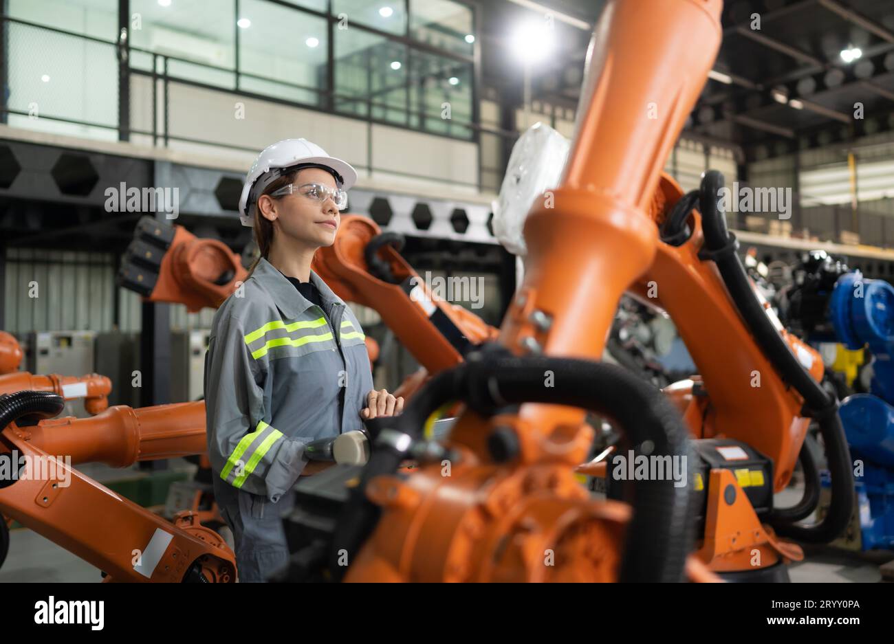 After installing a program on the robotic arm, a female engineer with a robotic arm controller performs a test run. Stock Photo