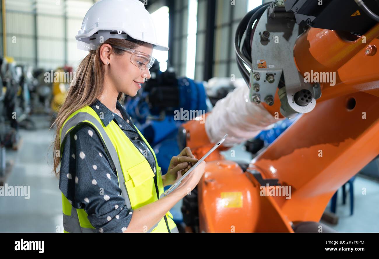 A female engineer installs a program on a robotics arm in a robot warehouse. And test the operation before sending the machine t Stock Photo