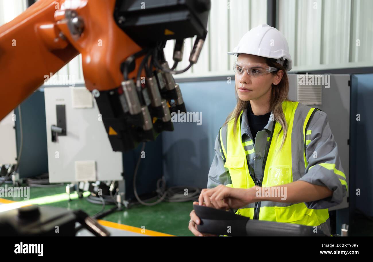 After installing a program on the robotic arm, a female engineer with a robotic arm controller performs a test run. Stock Photo