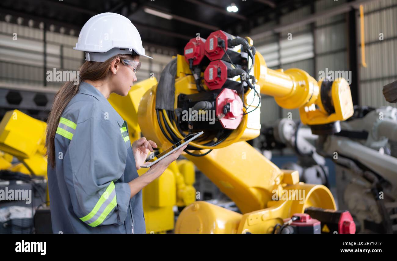 A female engineer installs a program on a robotics arm in a robot warehouse. And test the operation before sending the machine t Stock Photo