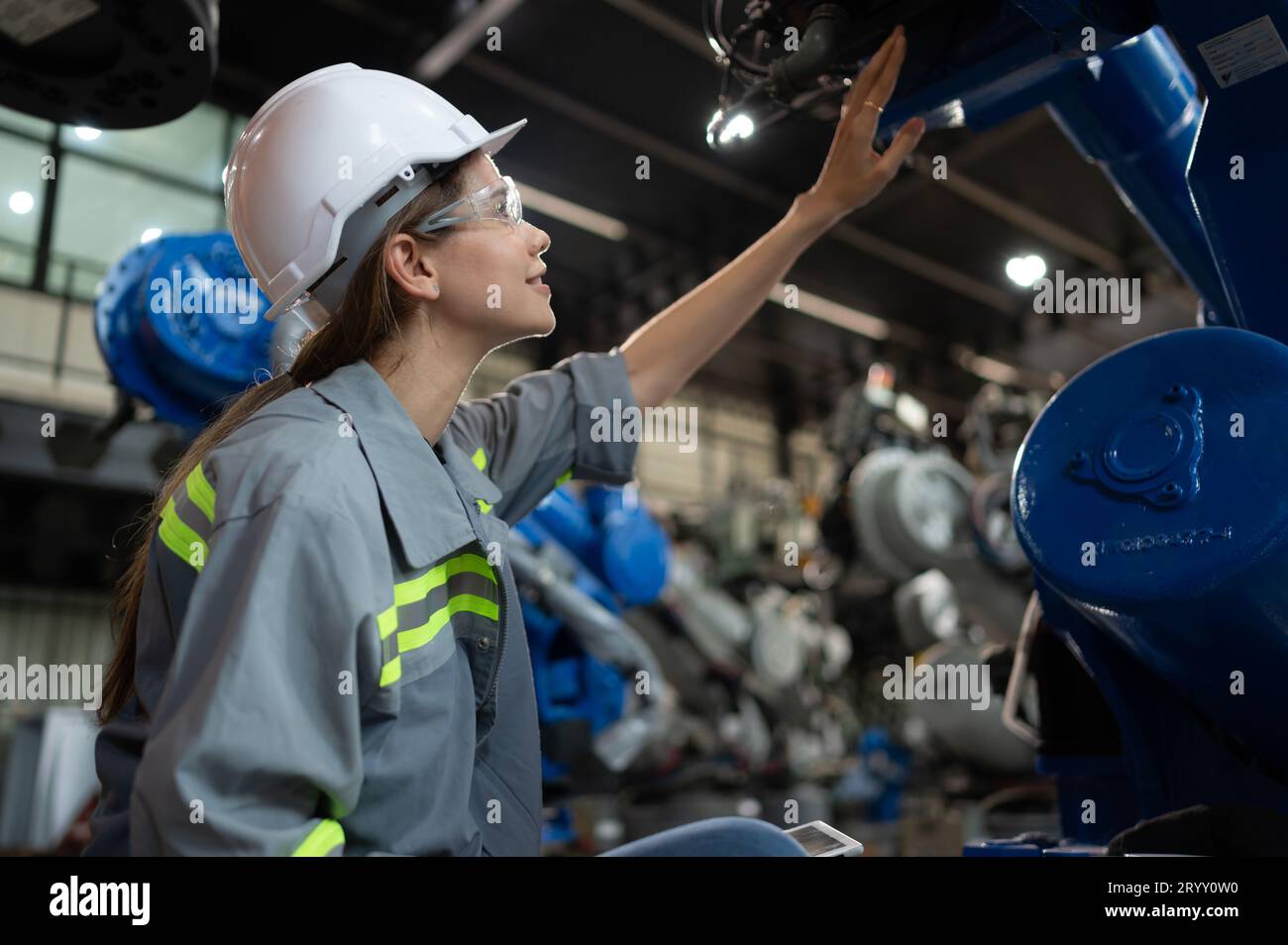 A female engineer installs a program on a robotics arm in a robot warehouse. And test the operation before sending the machine t Stock Photo