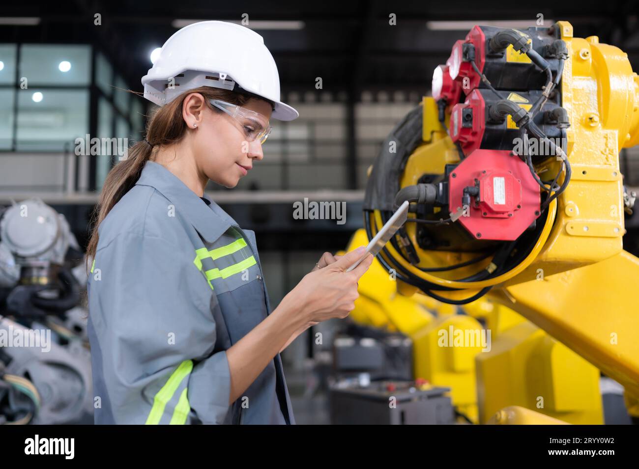 A female engineer installs a program on a robotics arm in a robot warehouse. And test the operation before sending the machine t Stock Photo