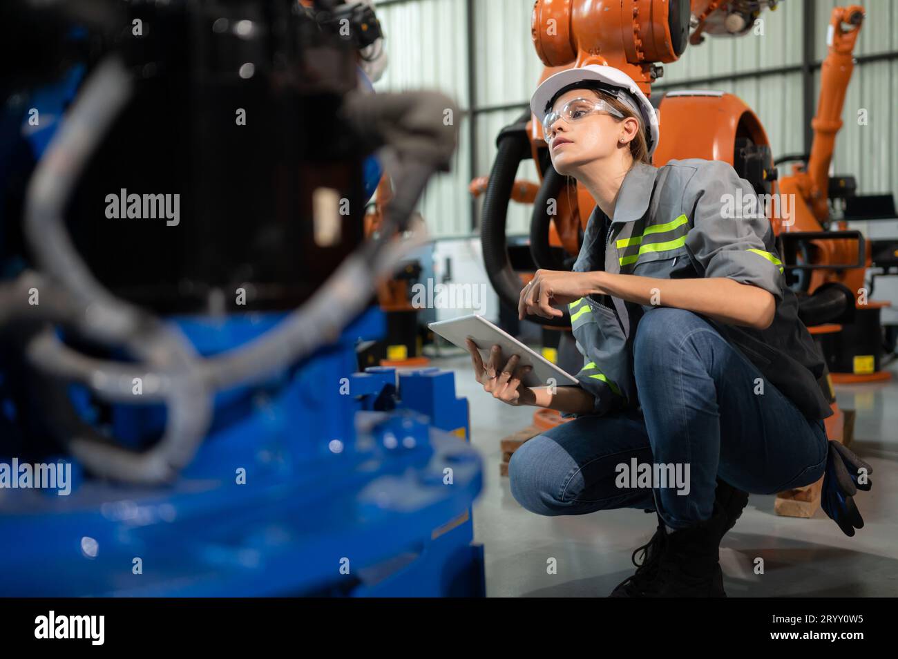 A female engineer installs a program on a robotics arm in a robot warehouse. And test the operation before sending the machine t Stock Photo