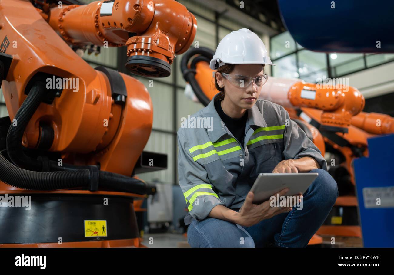 A female engineer installs a program on a robotics arm in a robot warehouse. And test the operation before sending the machine t Stock Photo