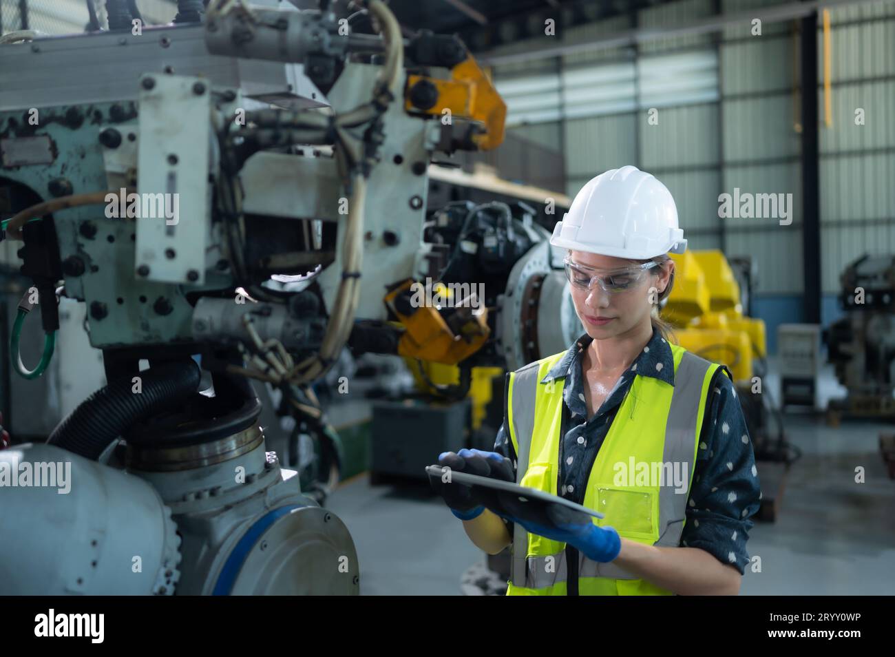 A female engineer installs a program on a robotics arm in a robot warehouse. And test the operation before sending the machine t Stock Photo