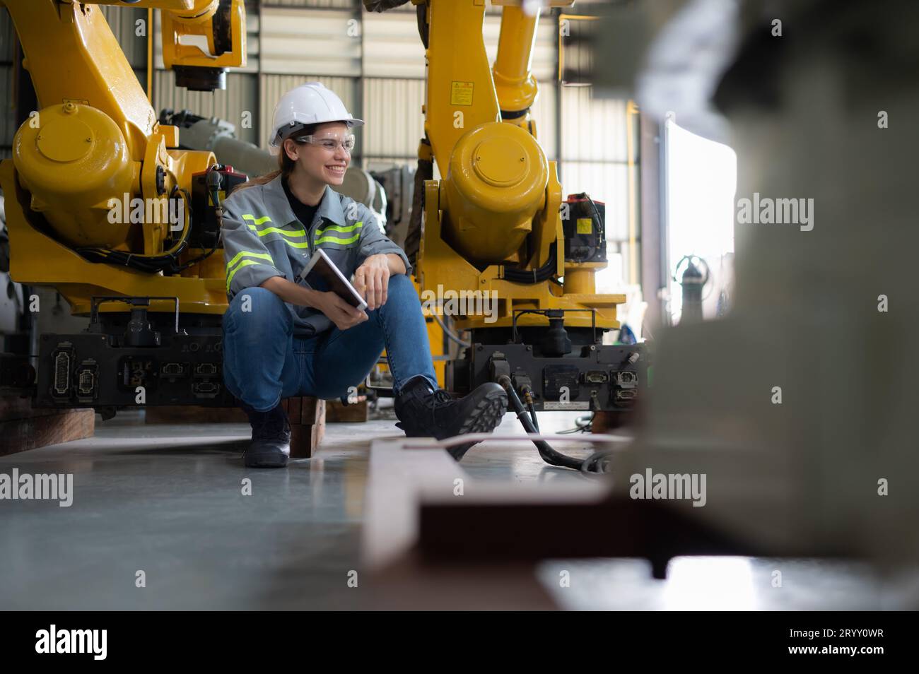 A female engineer installs a program on a robotics arm in a robot warehouse. And test the operation before sending the machine t Stock Photo