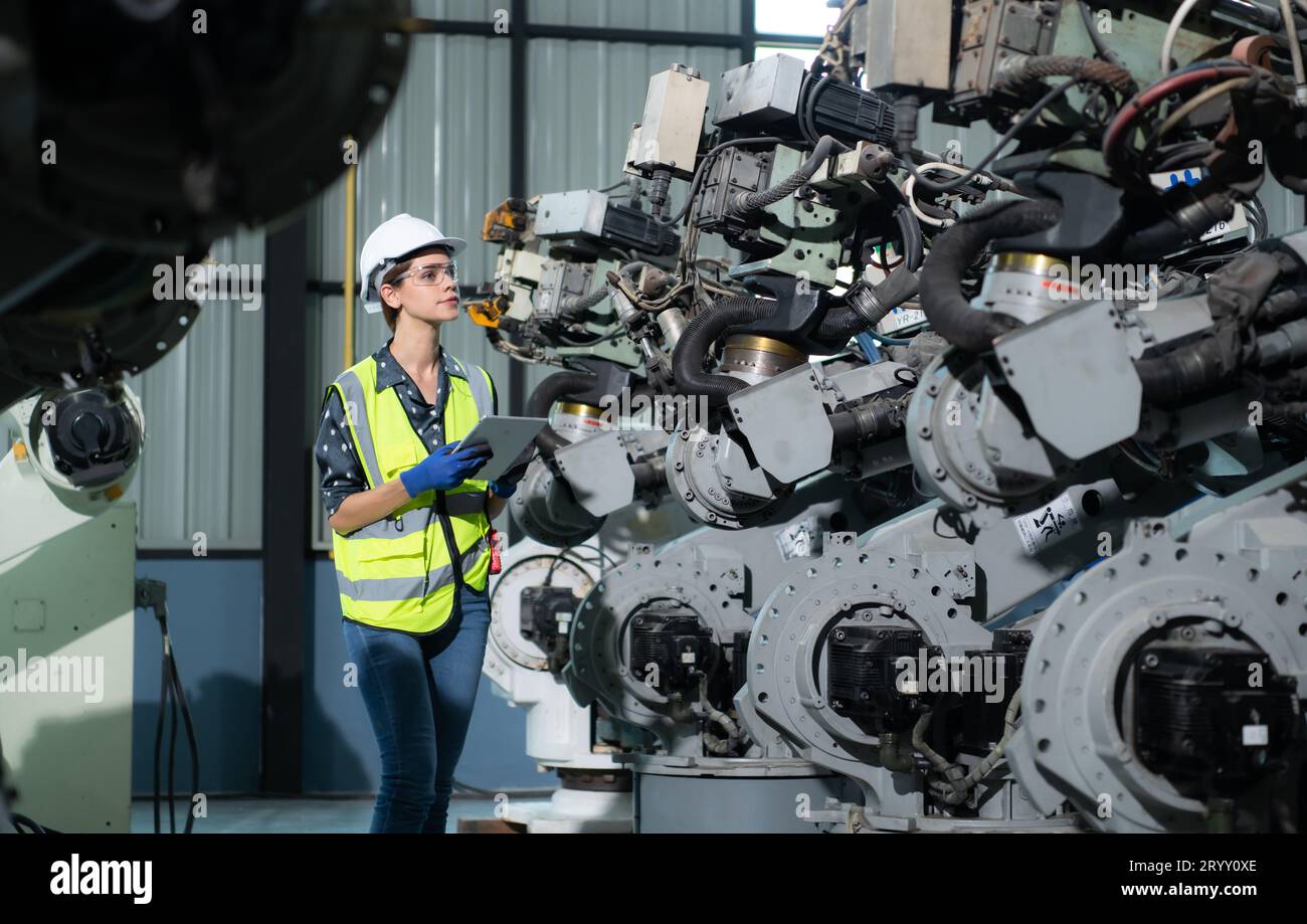 A female engineer installs a program on a robotics arm in a robot warehouse. And test the operation before sending the machine t Stock Photo