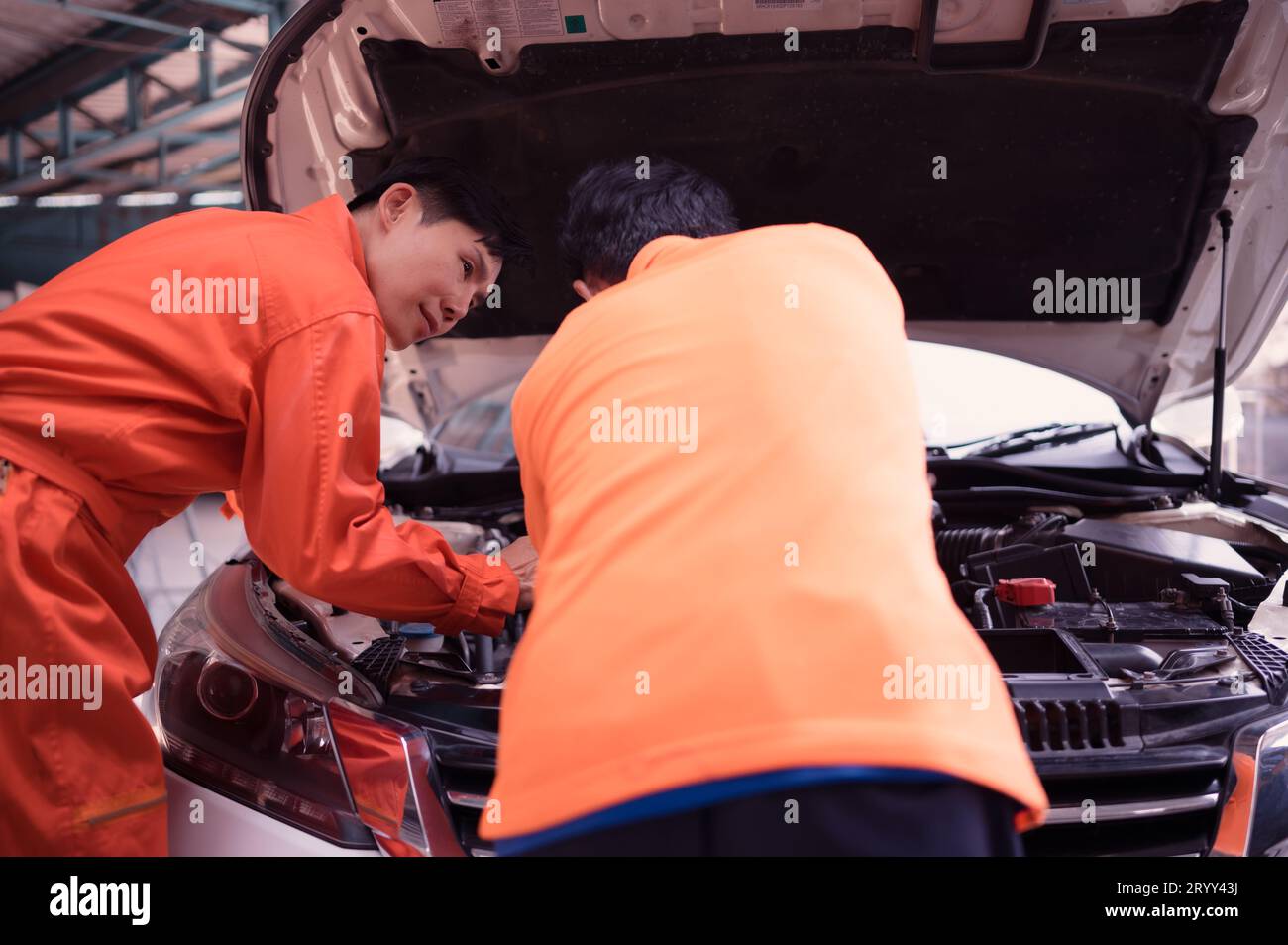 Both of auto mechanics are inspecting the engine of a customer's car being brought in for repair at a garage. Stock Photo