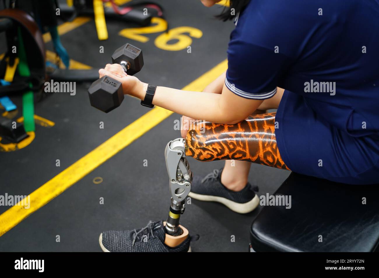 Young female with one prosthetic leg warms up by lifting light weights. Concept of living a woman's life with a prosthetic limb. Stock Photo