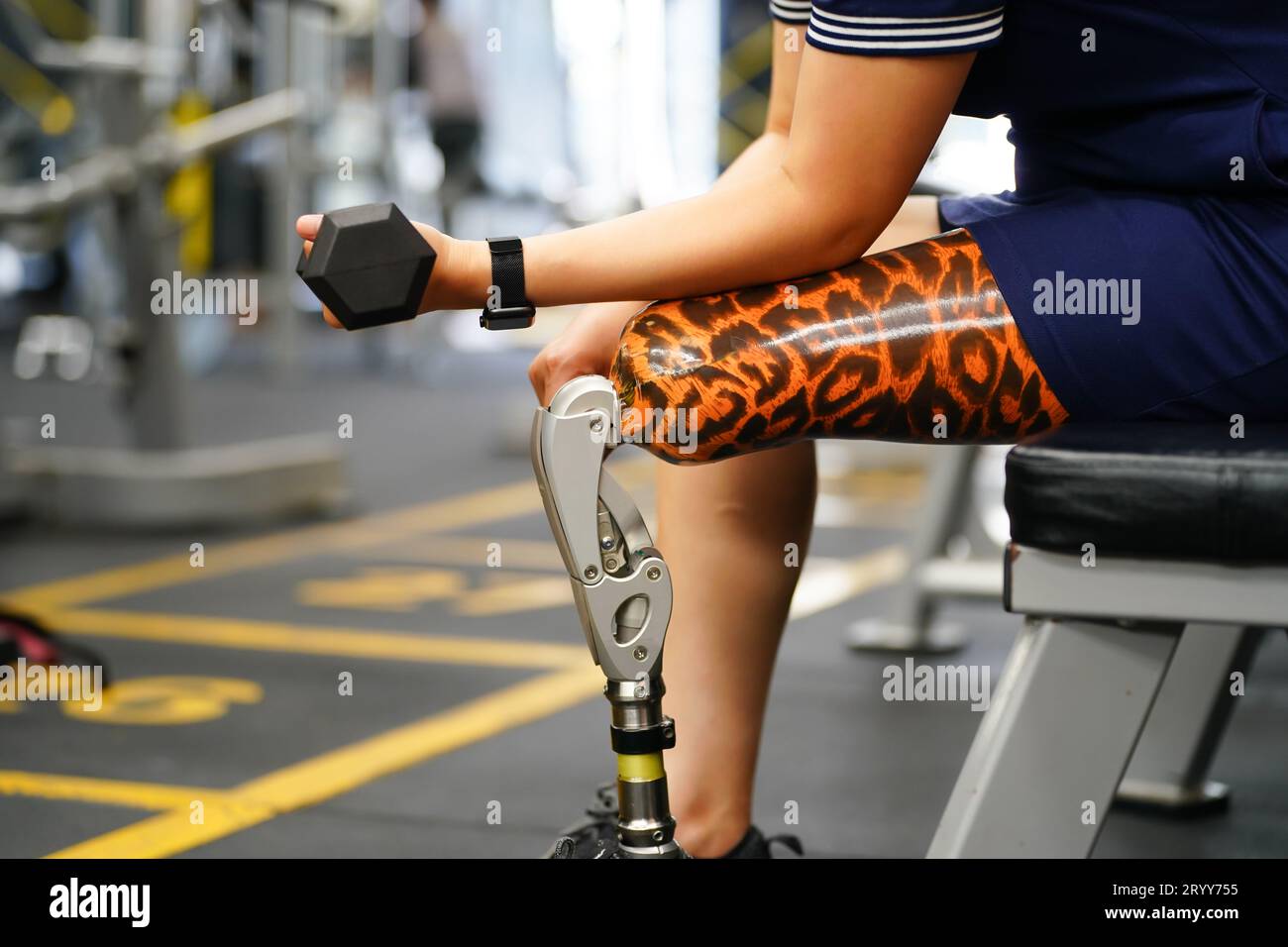 Young female with one prosthetic leg warms up by lifting light weights. Concept of living a woman's life with a prosthetic limb. Stock Photo