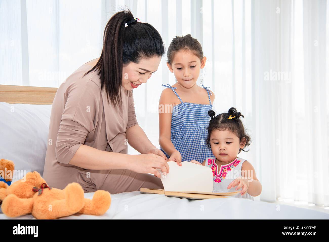Asian mother teaching mixed raced girls daughter to reading books in their house. Quarantine in home concept. Happy family theme Stock Photo