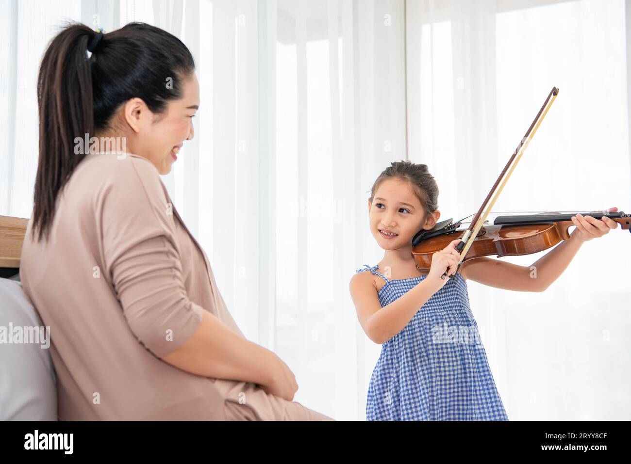 Girl playing violin with her pregnant mother for lullaby newborn in mother belly. Musical and entertainment concept. Stock Photo