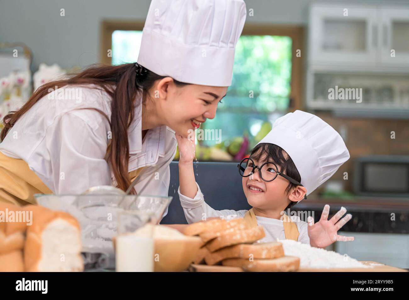 Cute little Asian boy painting beautiful woman face with dough flour