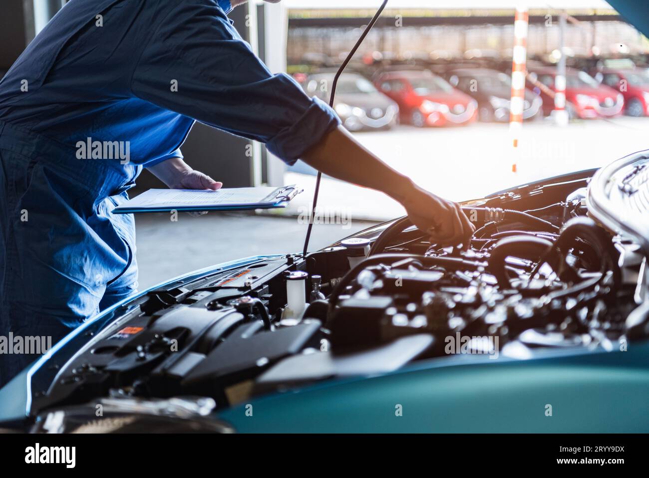 Car mechanic holding clipboard and checking to maintenance vehicle by customer claim order in auto repair shop garage. Engine re Stock Photo