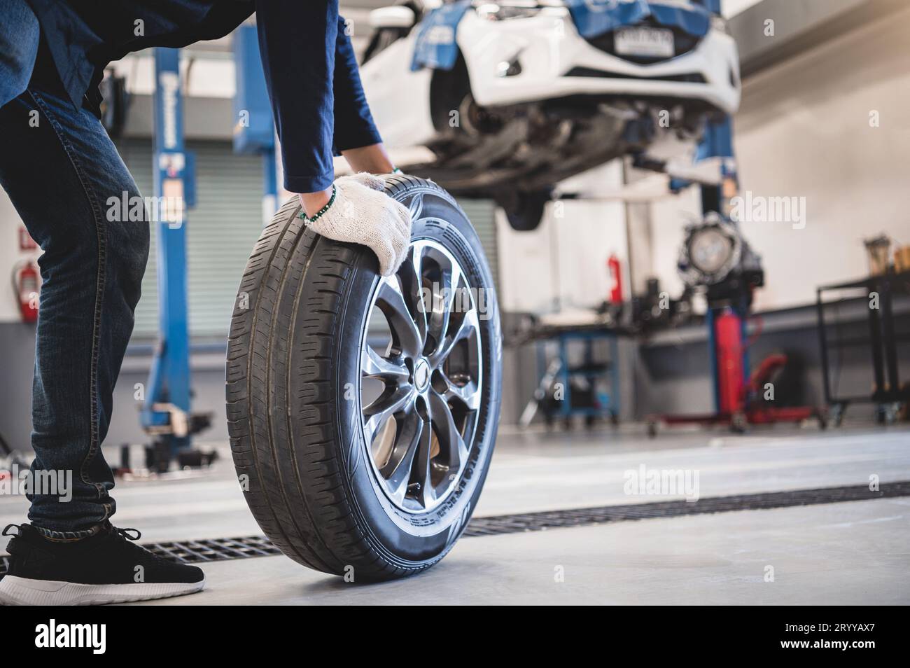Male mechanic hold and rolling tire at repairing service garage background. Technician man replacing winter and summer tyre for Stock Photo