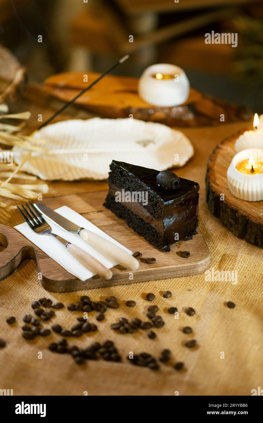 A slice of chocolate cake elegantly presented with cutlery, candles, and incense, without coffee. Emphasis on atmospheric and rustic aesthetics. Stock Photo