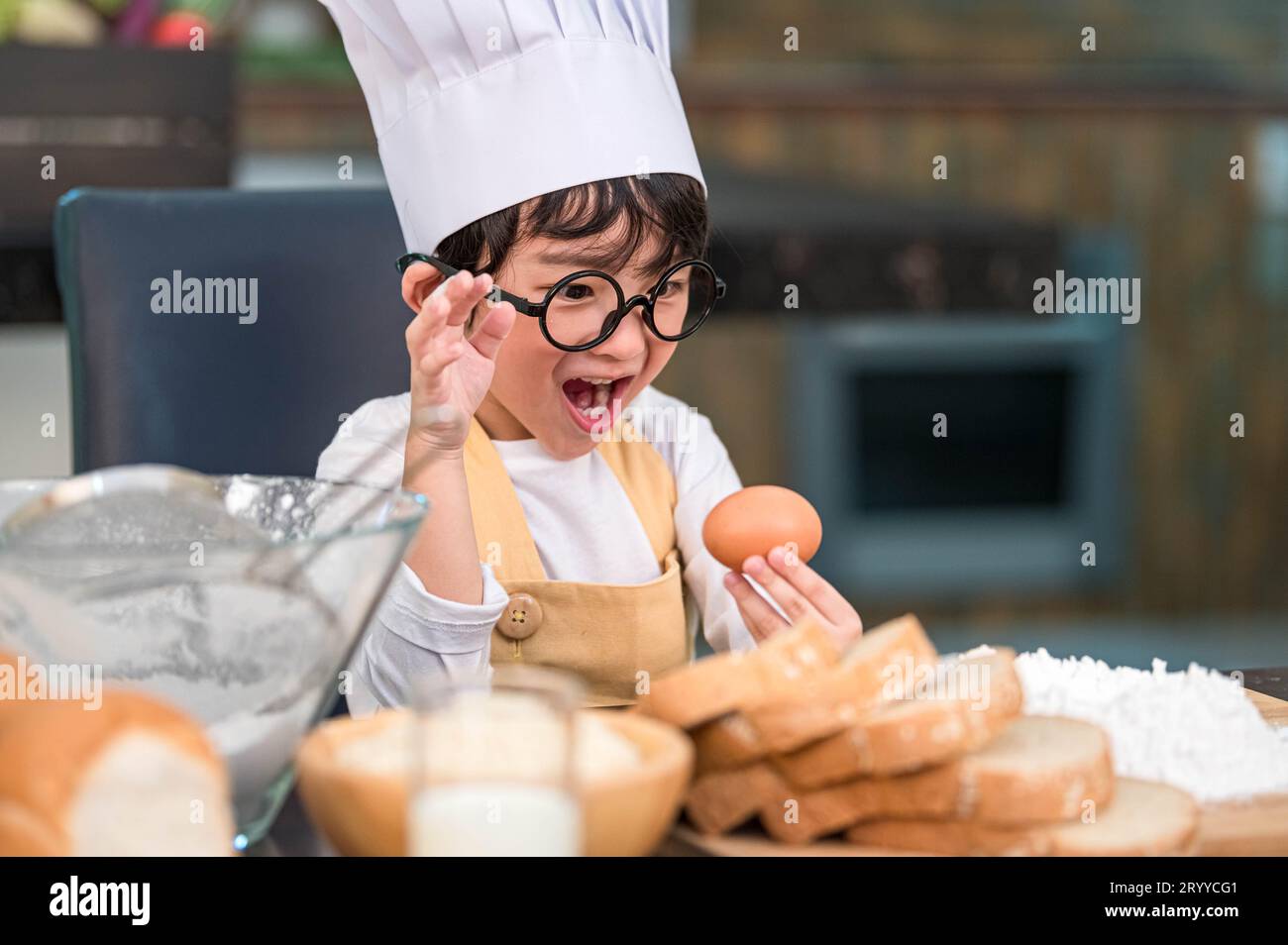 Portrait cute little Asian happy boy surprised and interested in cooking funny in home kitchen. People lifestyles and Family. Ho Stock Photo