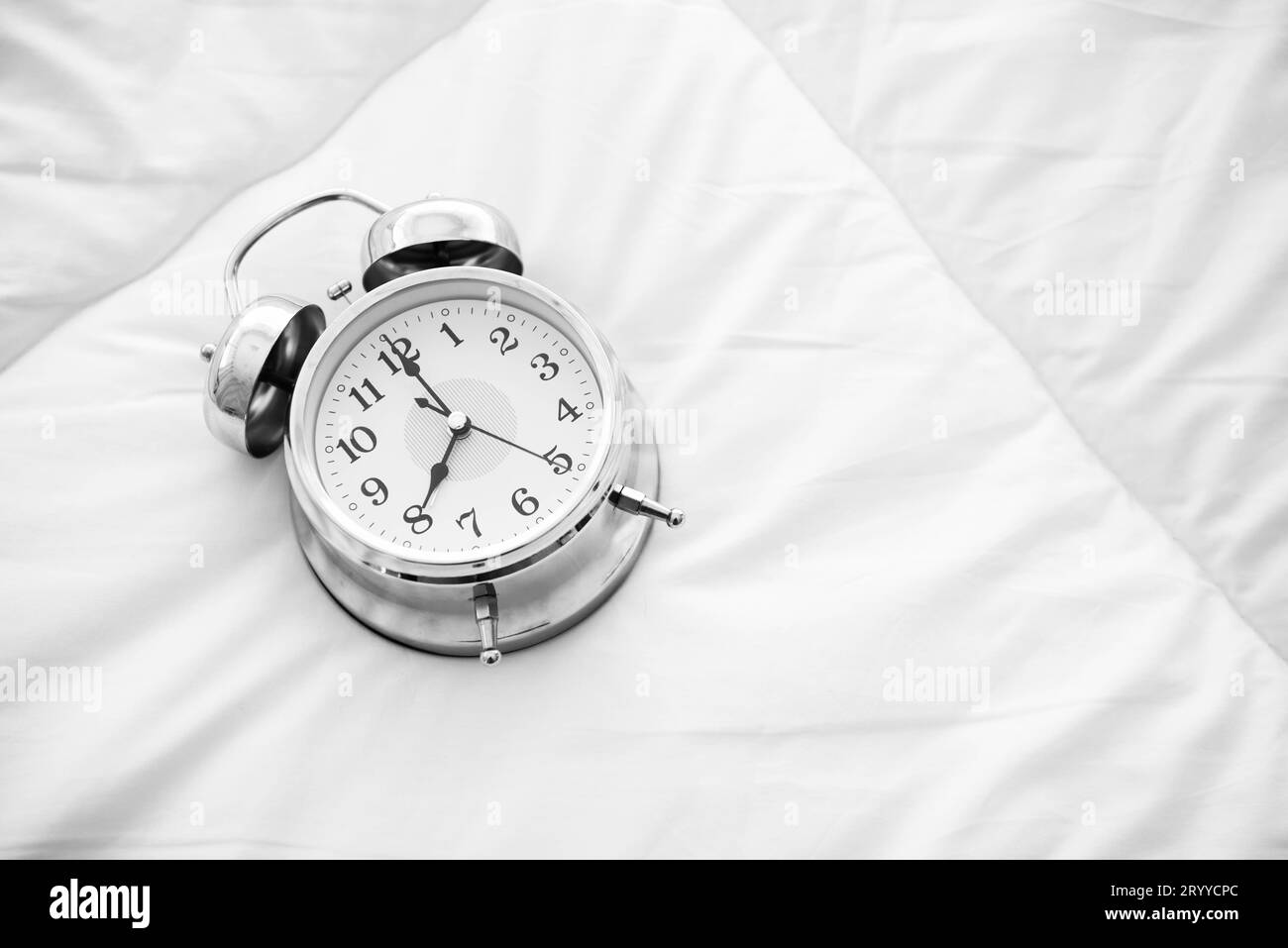 Ringing alarm clock on white bed sheet. Top view of object. 8 o clock