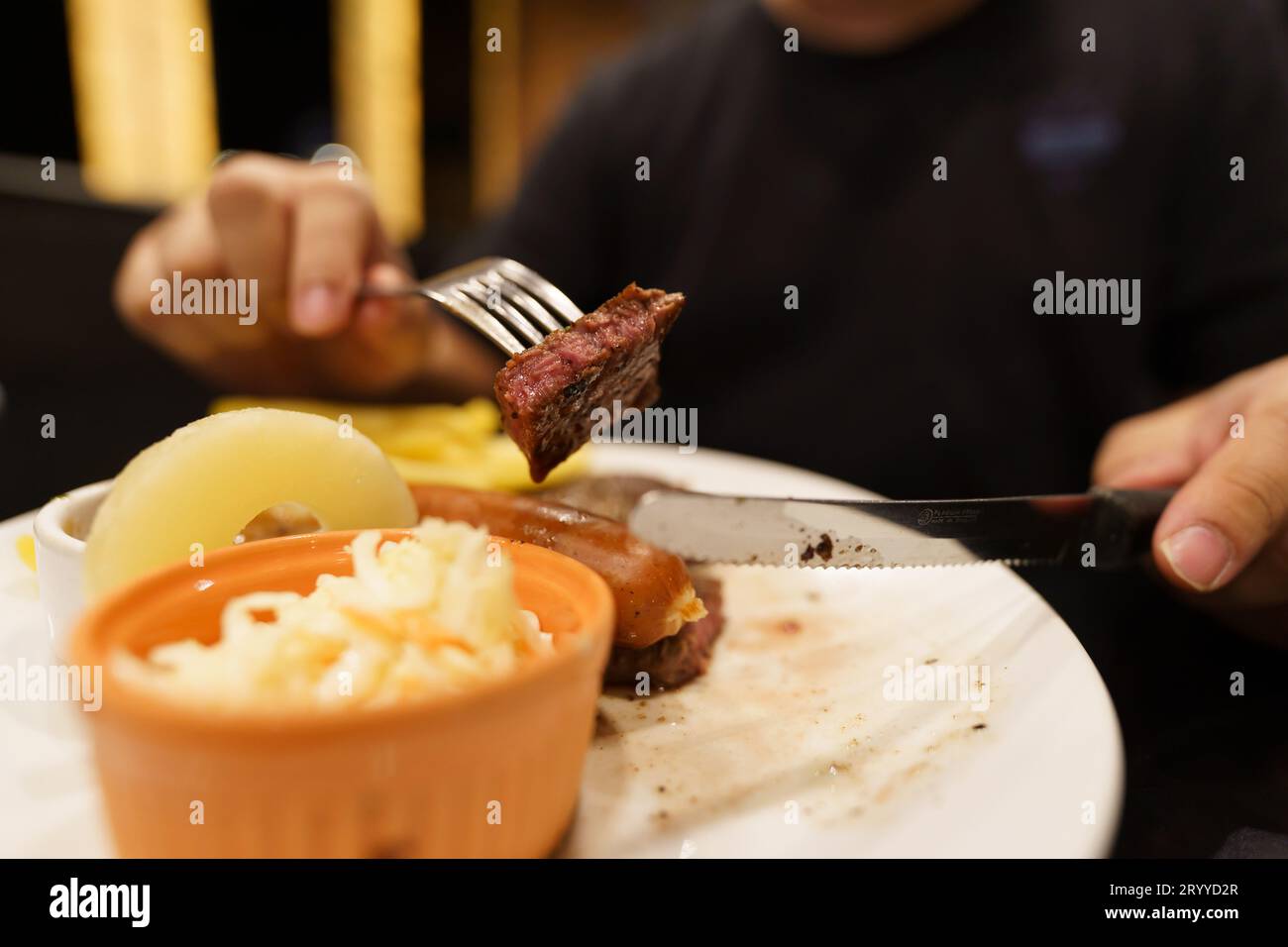 Man eating Grilled Meats stake from plate. hand holding knife and fork