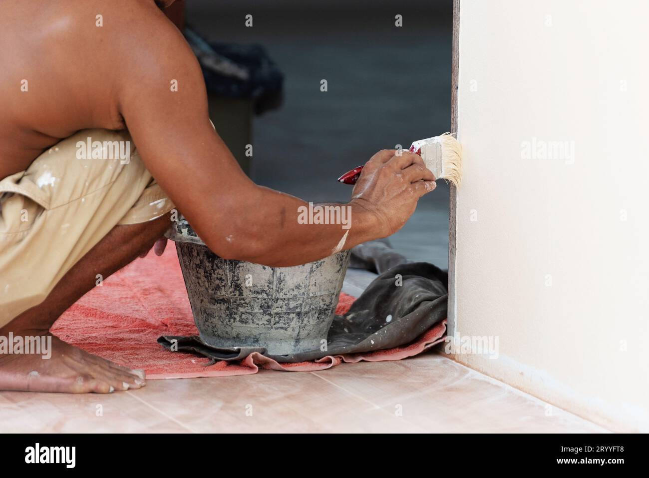 Close up of painter painting wall with brush and black paint bucket