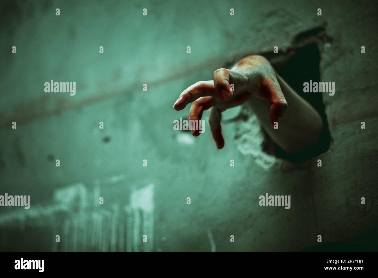 Zombie hand through the cracked wall. Horror and scary film concept. Halloween day theme. Green tone like ghost movie Stock Photo