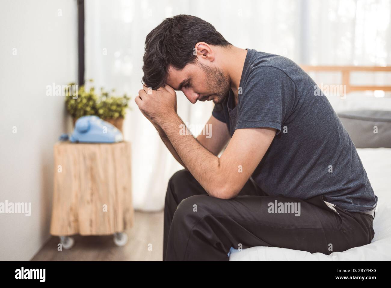 Worried man sitting on bed with hand on forehead in bedroom in serious
