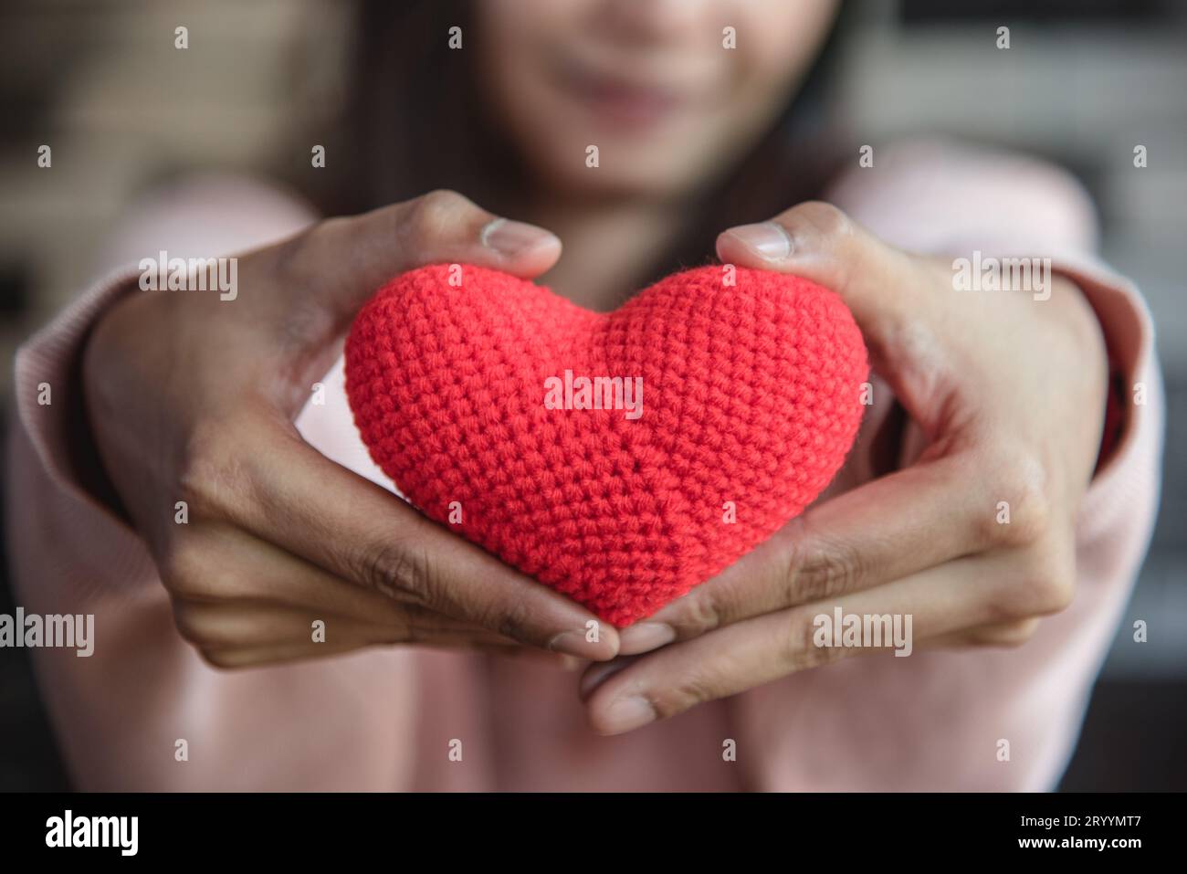 Big red yarn heart holding and giving to front by woman hand. Love and affection in Valentines day concept. Romantic object and Stock Photo