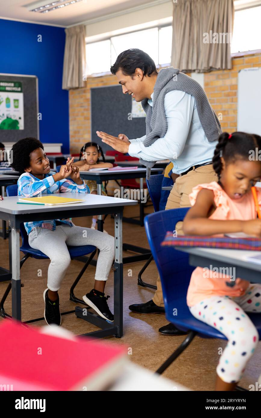 Diverse male teacher teaching school boy using sign language in class at elementary school Stock Photo