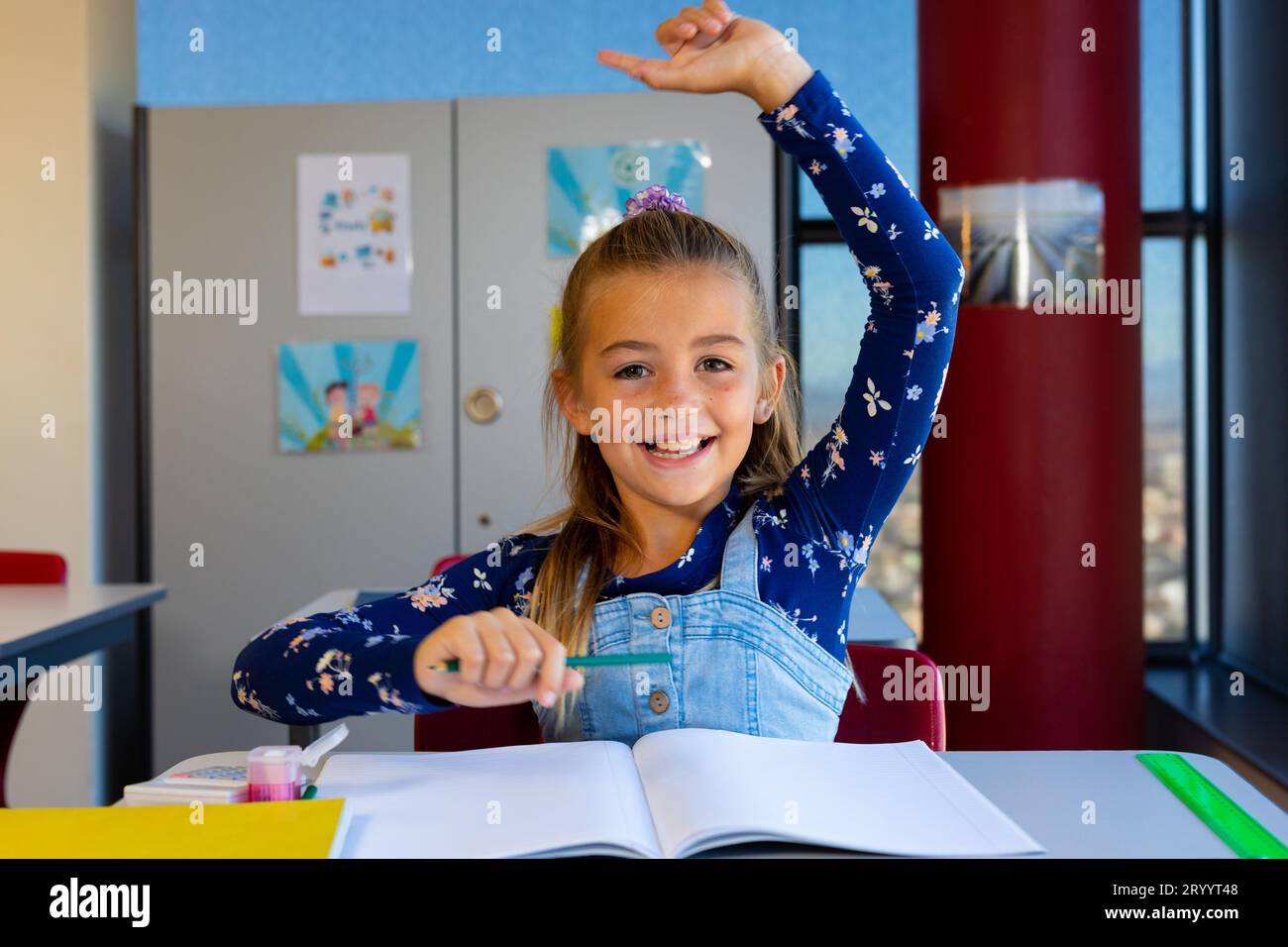 Portrait of caucasian schoolgirl sitting at desk raising hand in ...