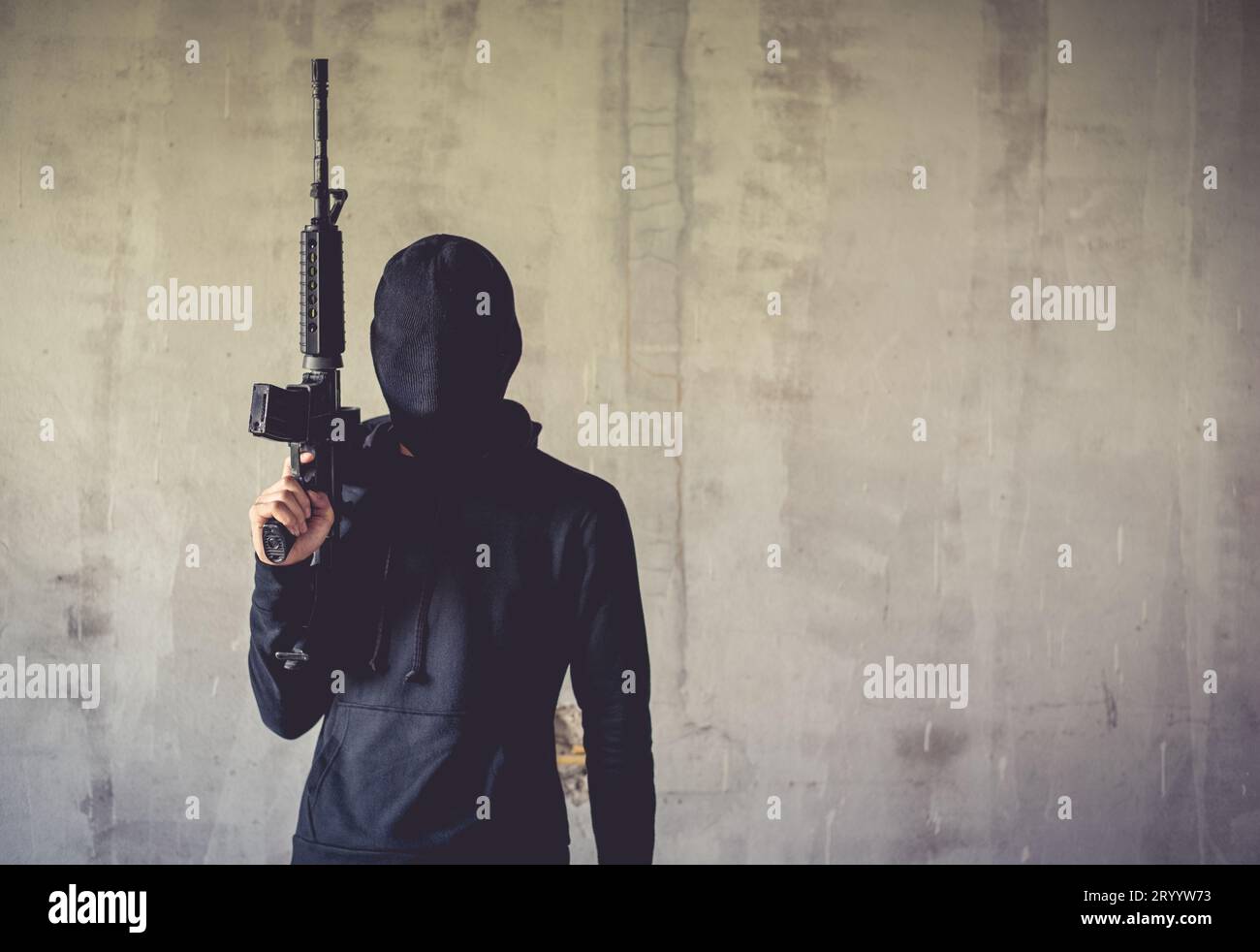 Terrorist holding rifle gun on grunge wall. Social issued theme. Terrorist and Robber concept. Police and Soldier theme. Social Stock Photo