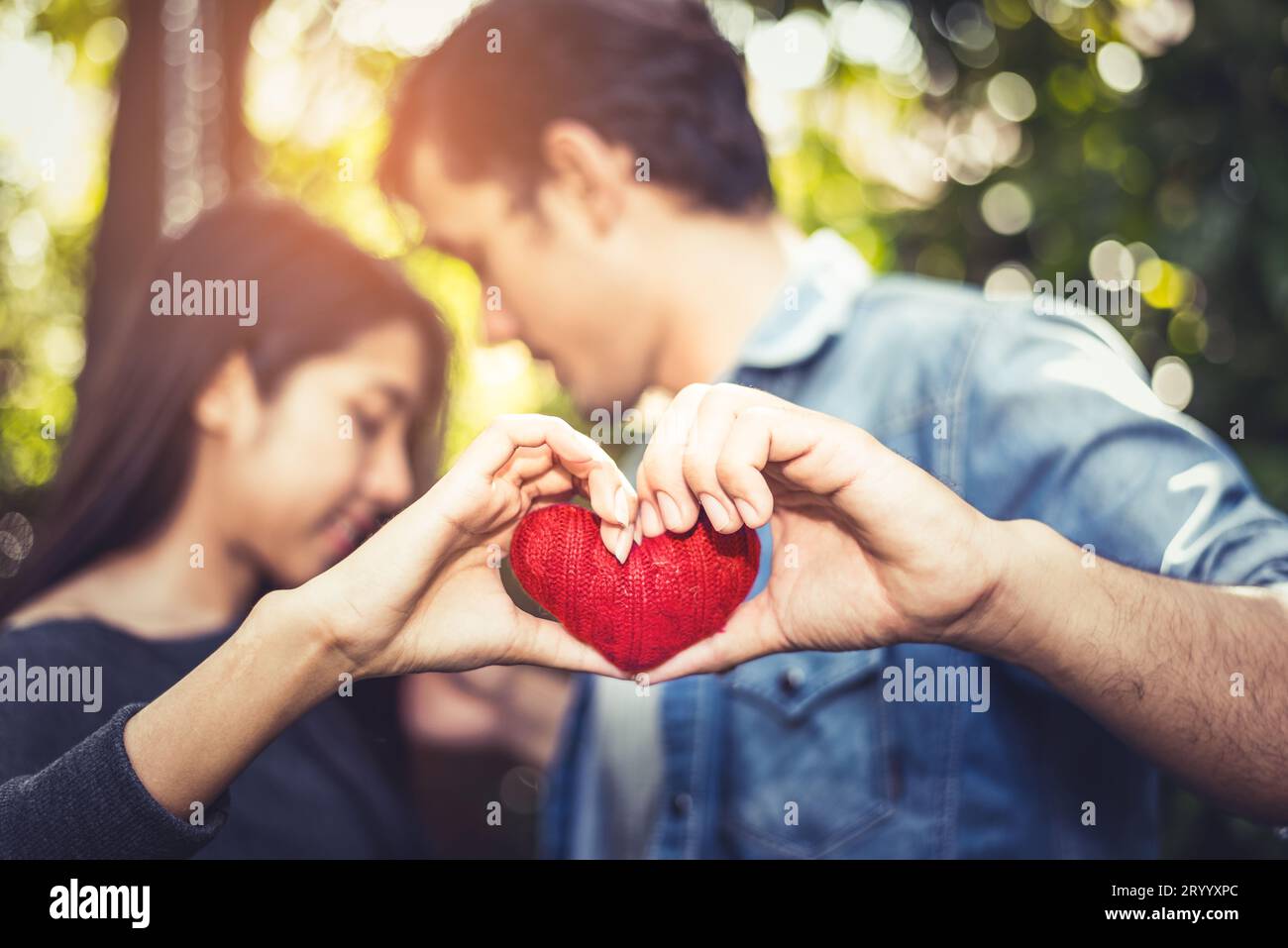 Two hands of young lovers or couple holding Red Heart yarn in middle at natural outdoor background for Valentines day. Holiday a Stock Photo