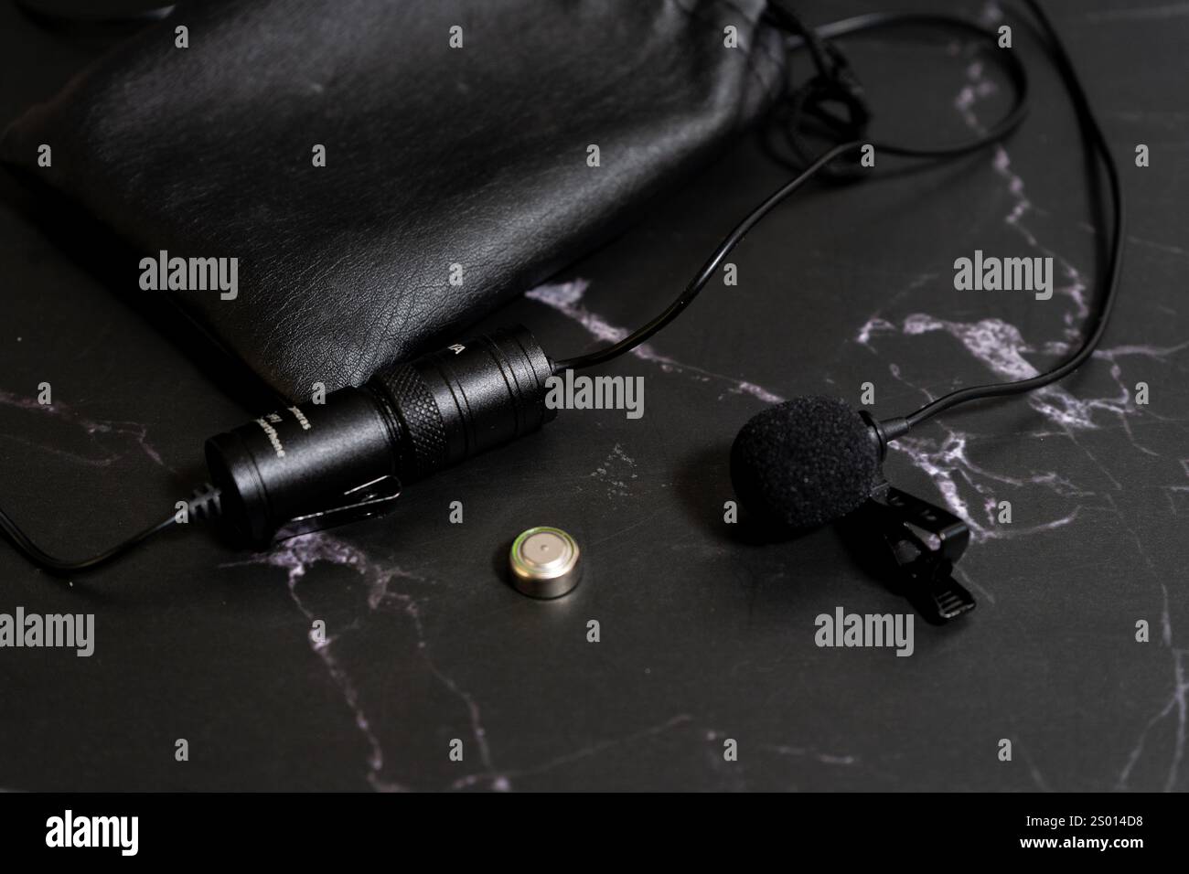 Lavalier microphone on a black background with a spare battery. Stock Photo