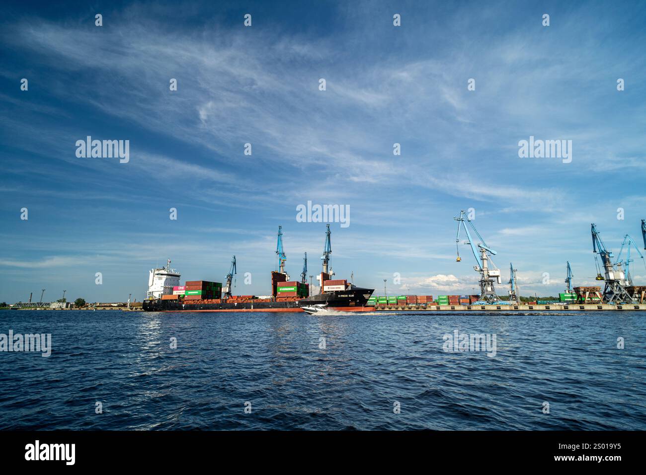 A cargo ship docked at a busy industrial port with cranes and shipping ...