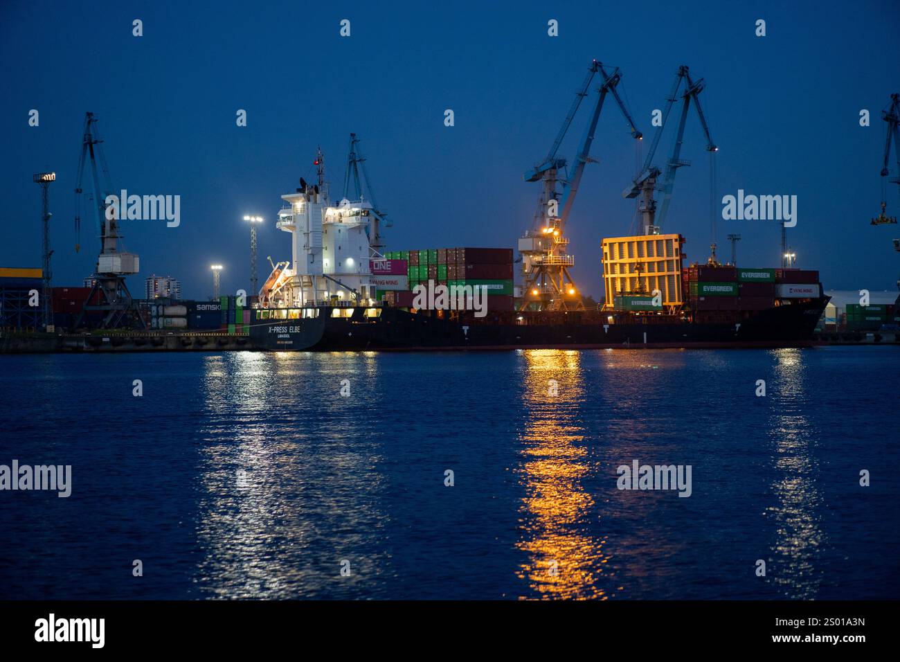 A cargo ship docked at twilight with cranes and stacked containers ...