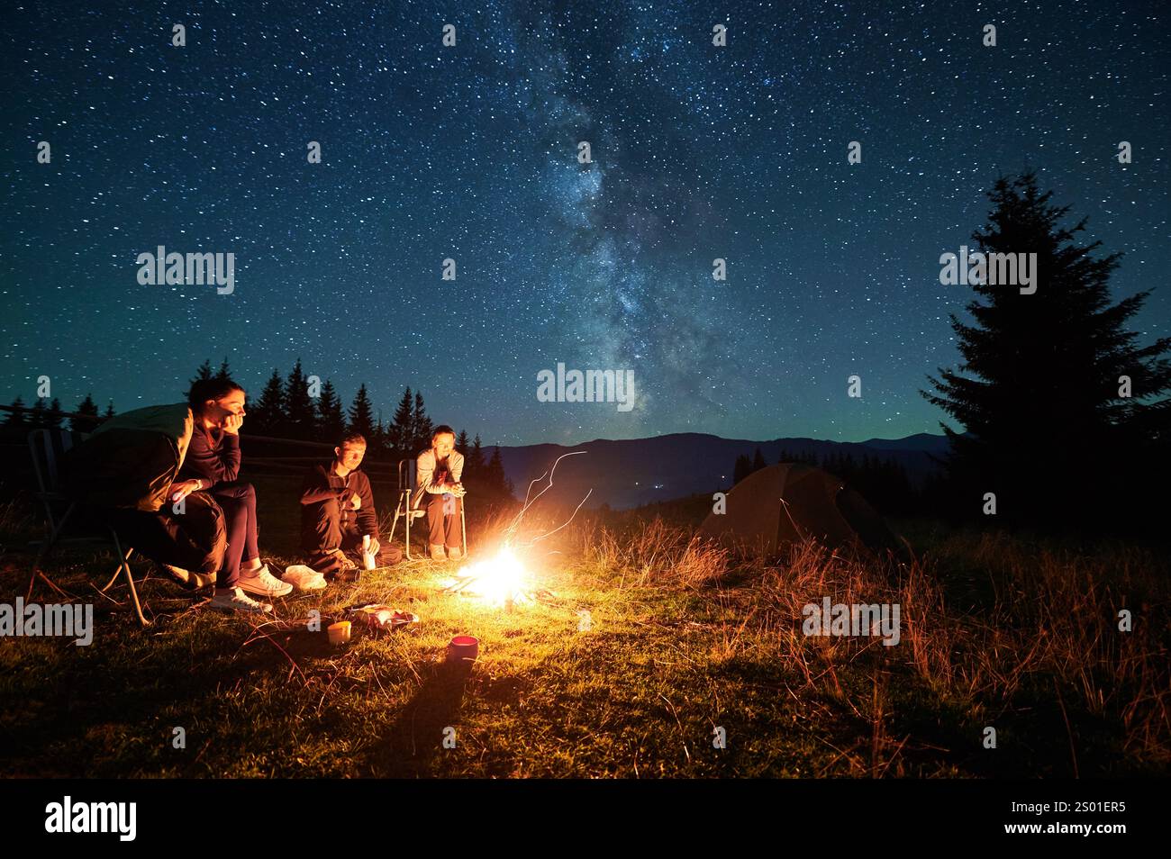 Group of friends sits around campfire under magnificent starry sky ...