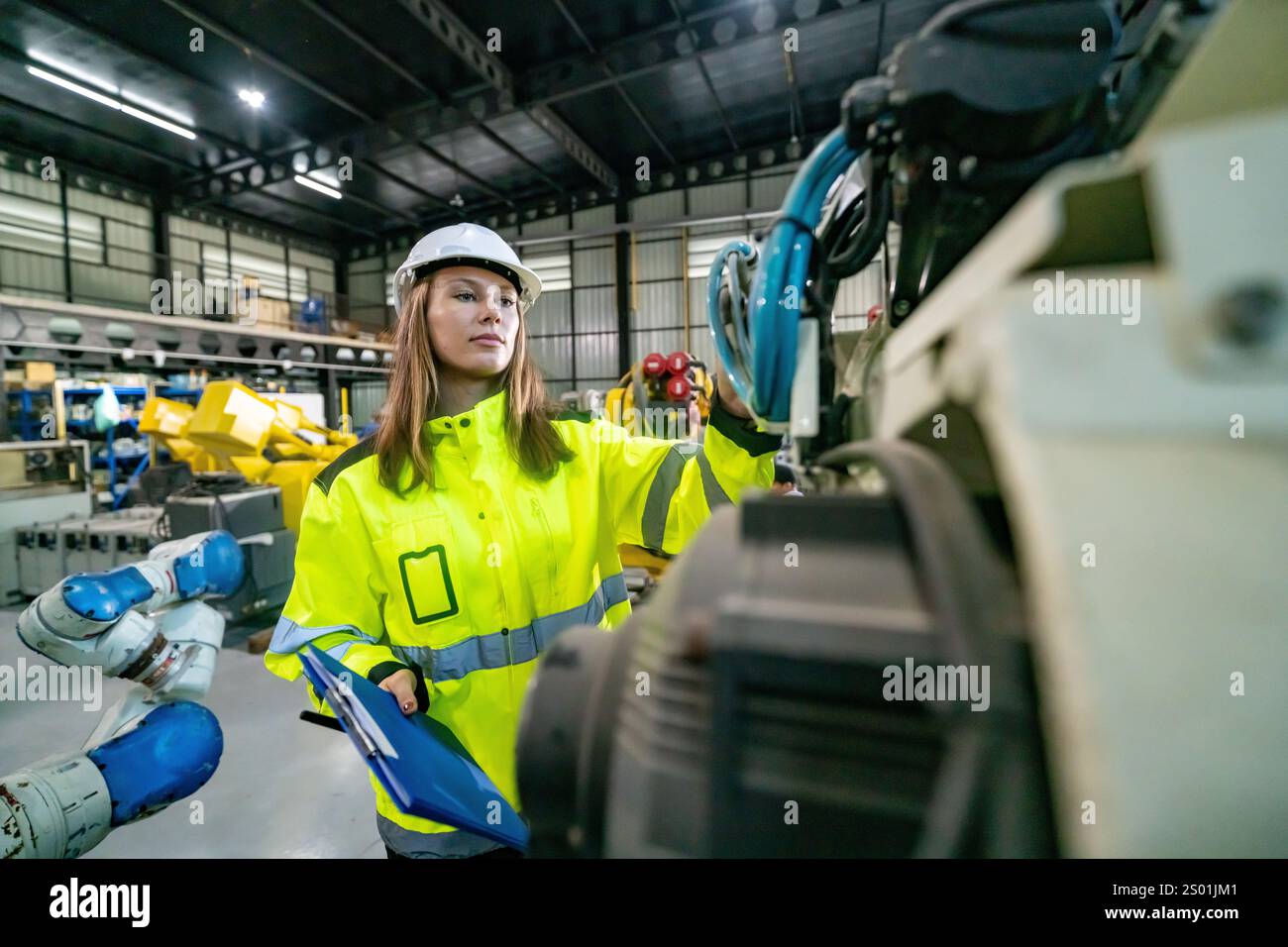 A skilled engineer in a high-visibility jacket examines robotic equipment. Stock Photo