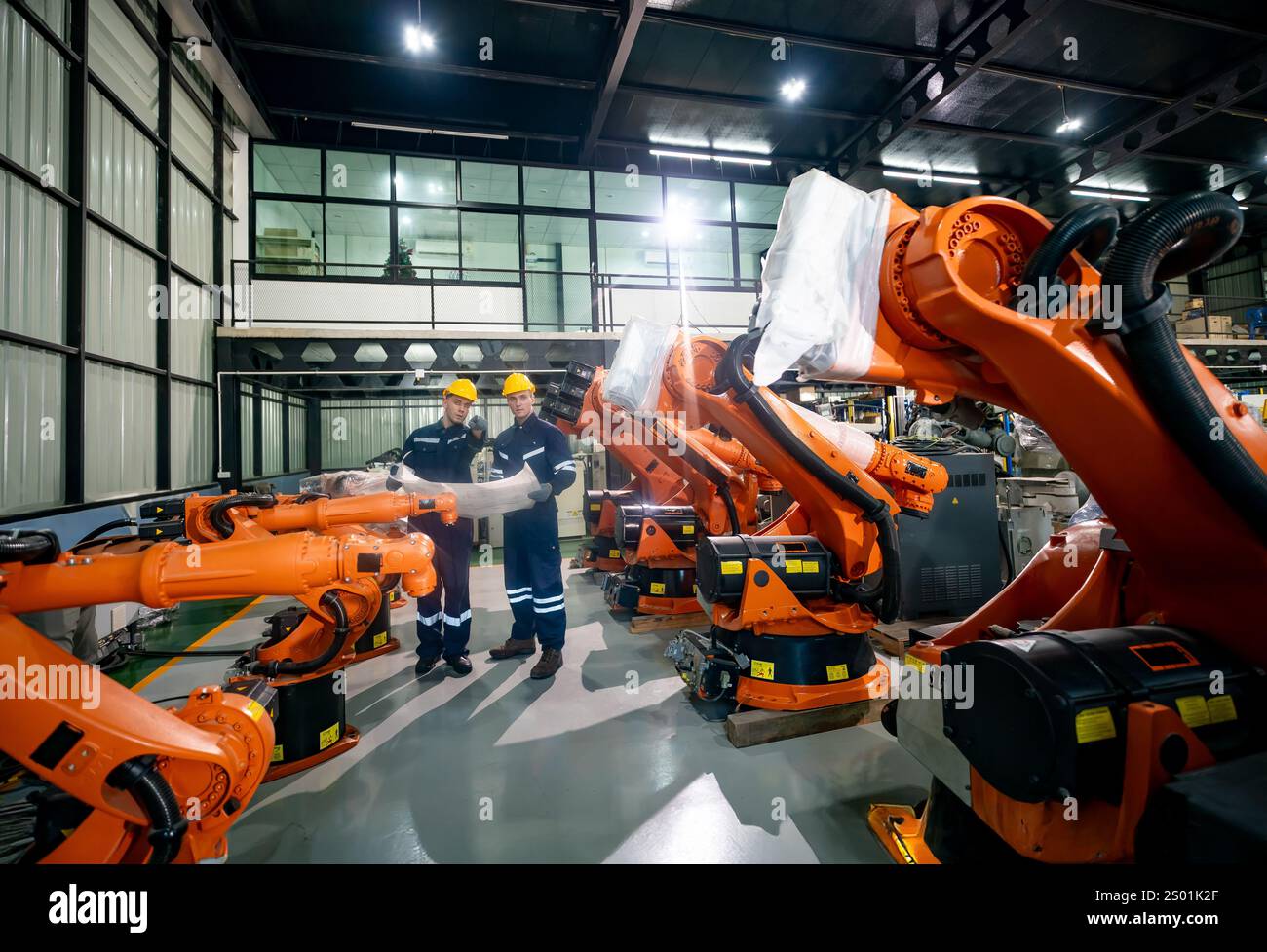 Two workers observe and manage robotic arms lined up in a modern ...