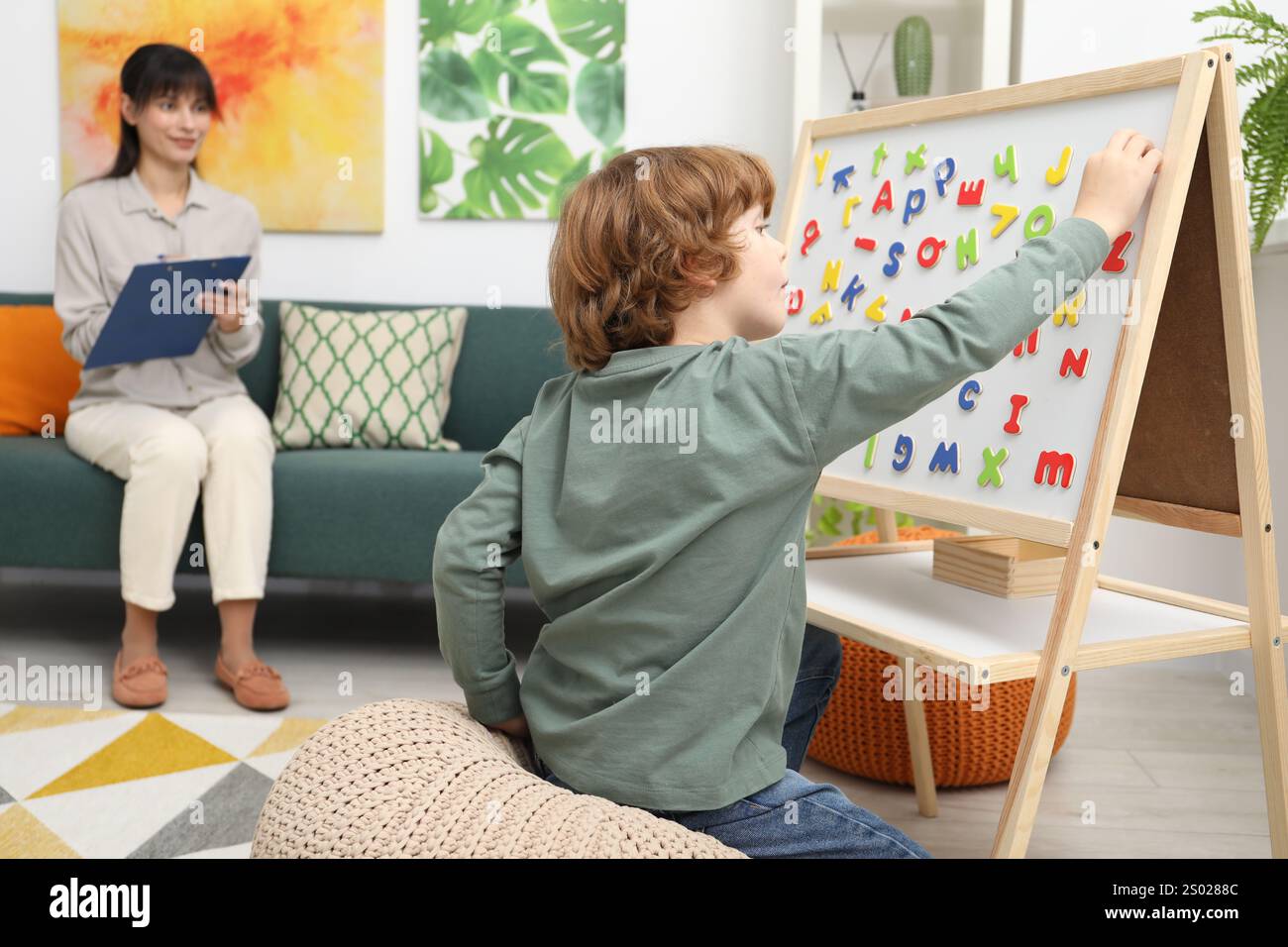 Boy assembling letters on magnetic board while psychologist taking ...